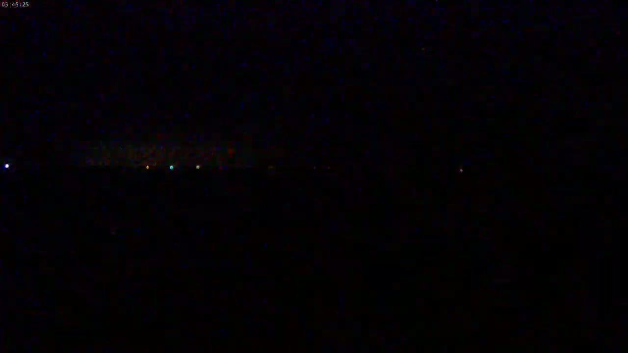 A dark, nighttime scene shows a distant line of faint lights on the horizon.