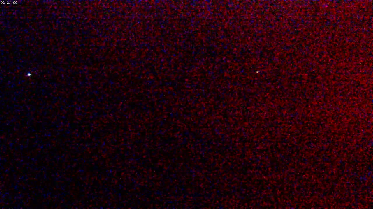 A nighttime image shows a dark sky speckled with a multitude of dim red and blue lights, and a single, bright white light.