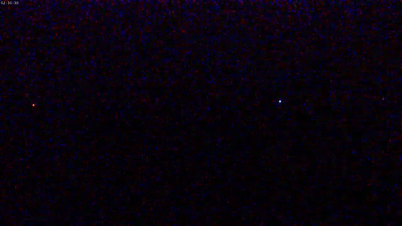 A nighttime sky shows a dark expanse speckled with numerous faint stars and three brighter celestial bodies, one reddish and two white.