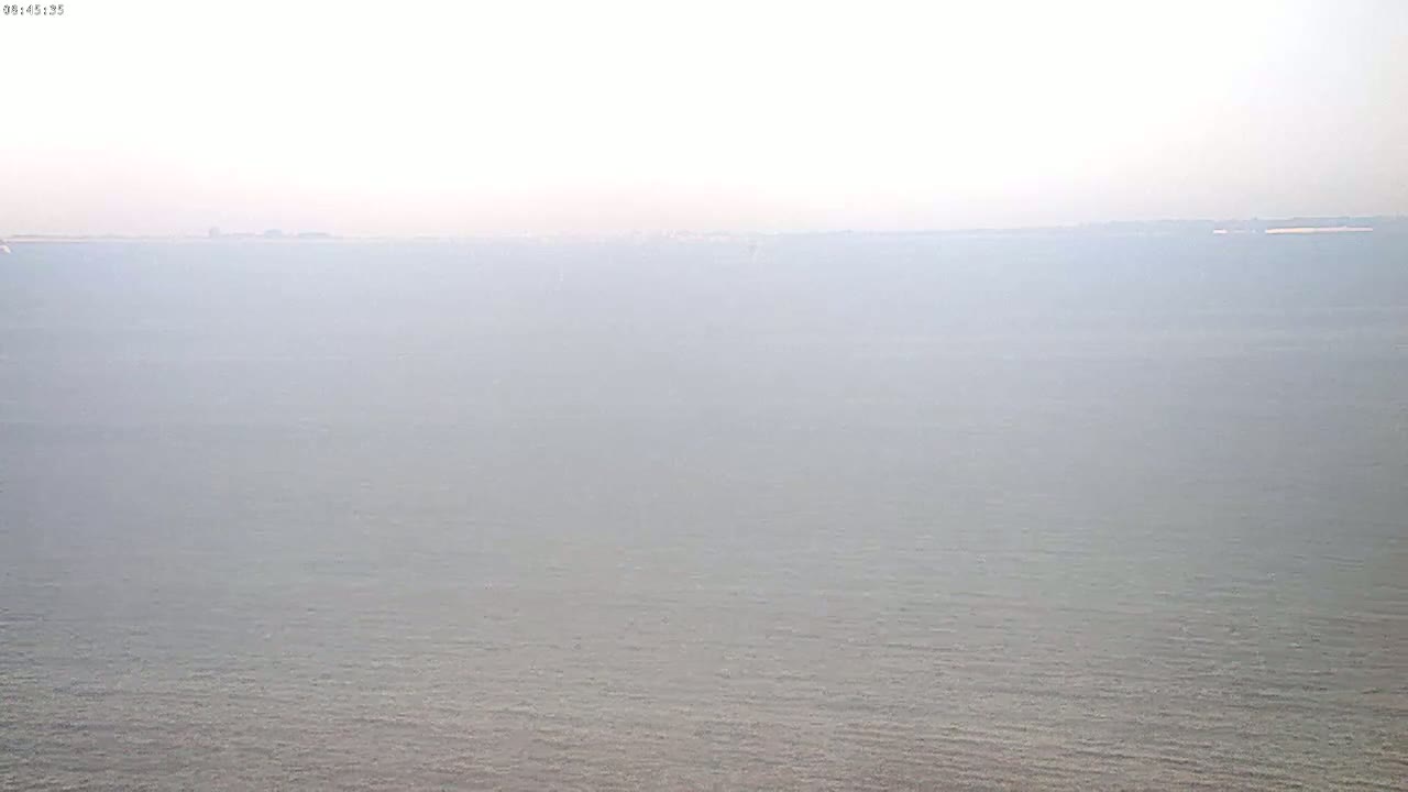 A hazy view of calm water extends to a distant, indistinct shoreline.