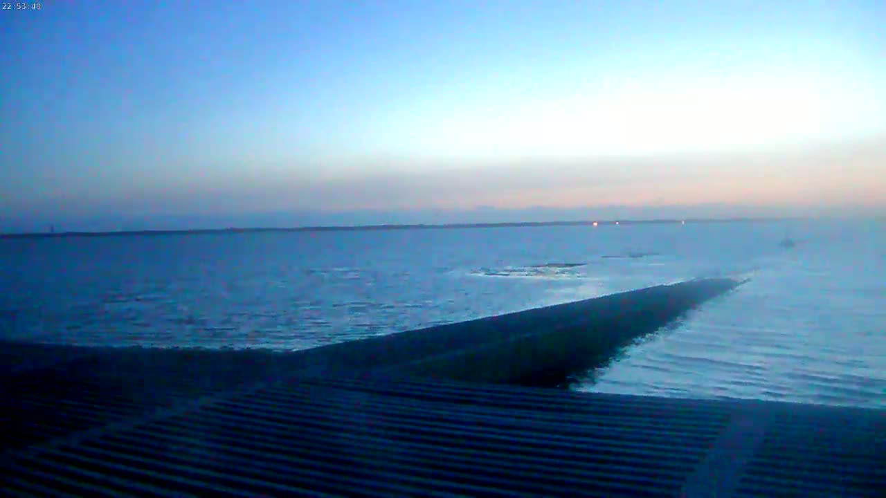 A long, dark structure extends into a calm, twilight-colored body of water under a clear, dusky sky.