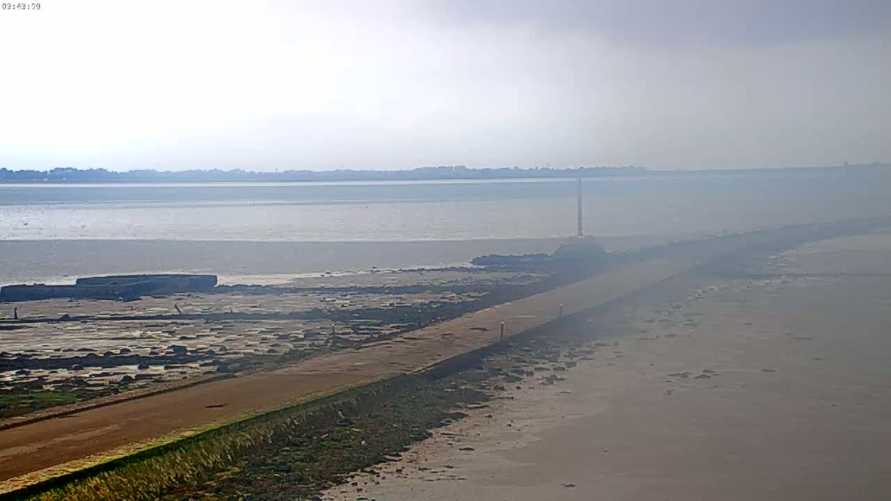 A hazy, light-colored road extends from the foreground into a calm body of water, which stretches to a distant shoreline.