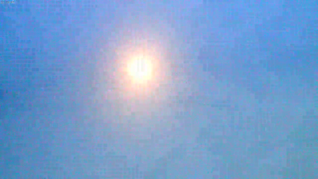 A bright sun shines in a hazy, light-blue sky.