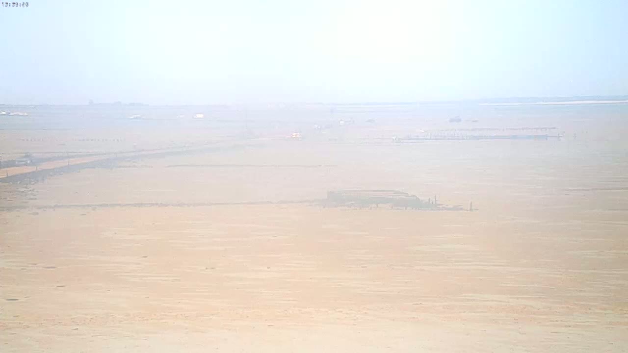 A hazy, light-colored expanse of land stretches to a distant horizon under a bright, mostly clear sky.