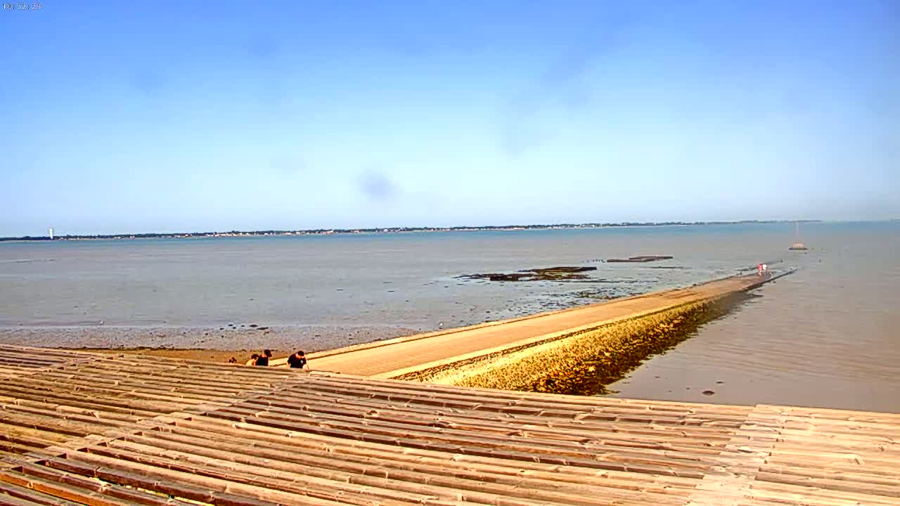 A long, narrow causeway extends from a tiered, wooden structure into a calm, light brown body of water under a clear blue sky.