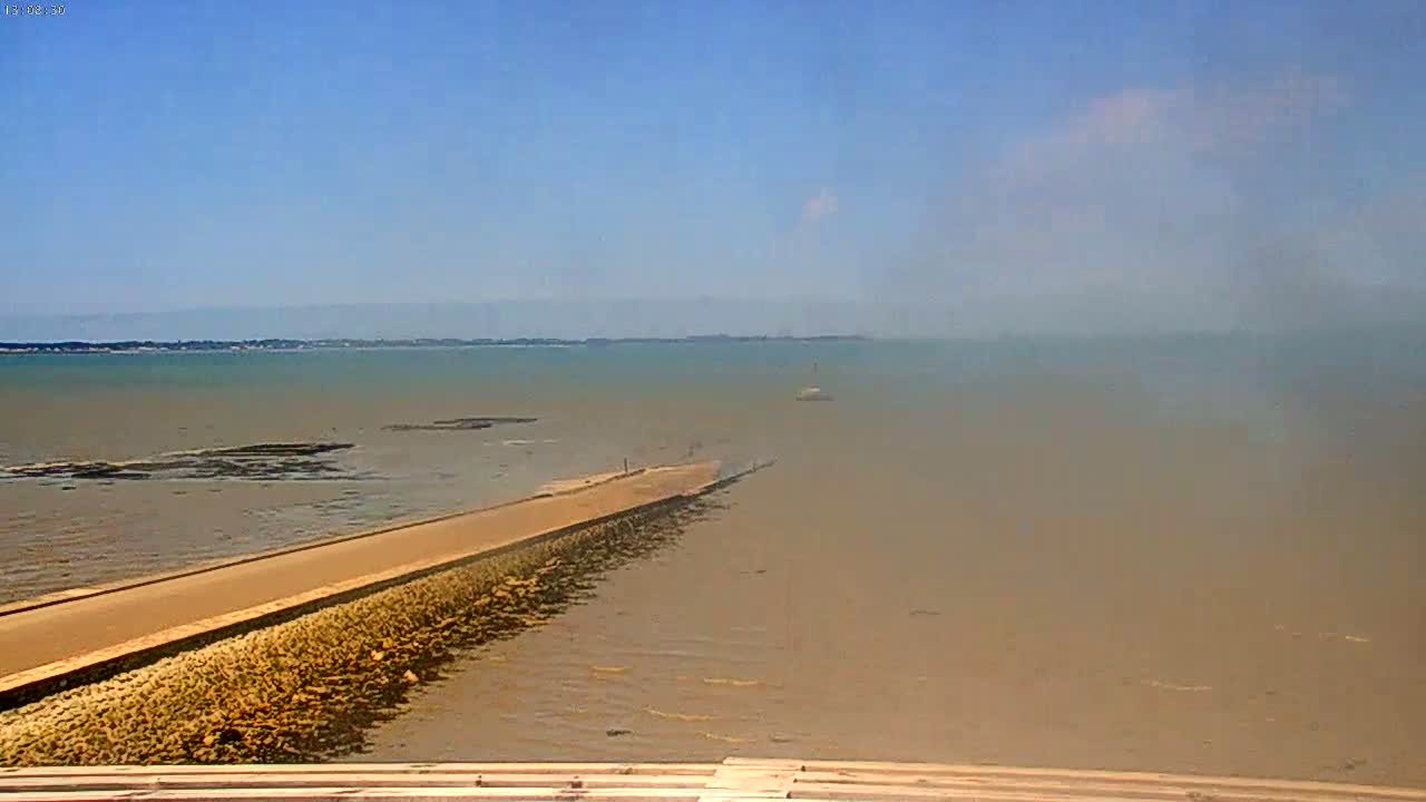 A long, narrow, light-brown path extends into a hazy, light-brown body of water under a mostly clear, light-blue sky.