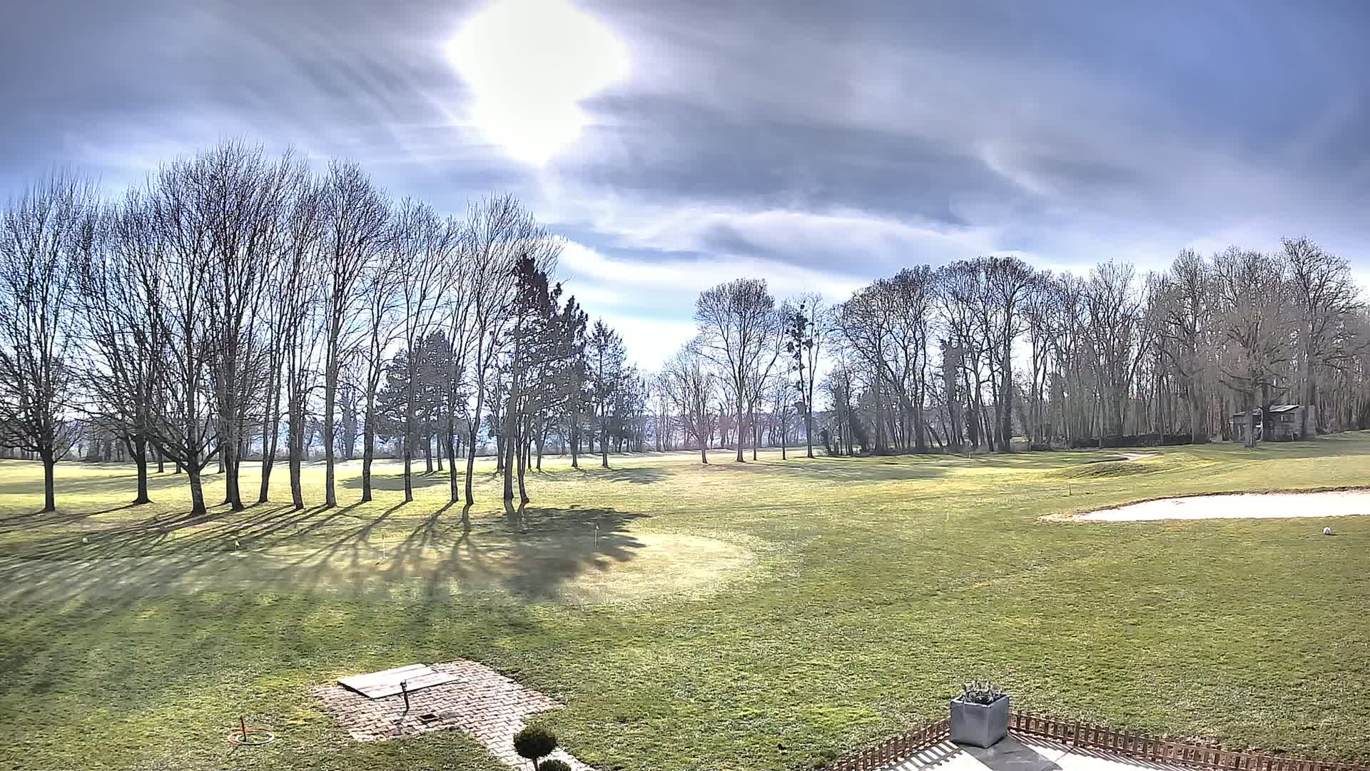 A sunny day on a golf course with leafless trees casting shadows on a grassy field.