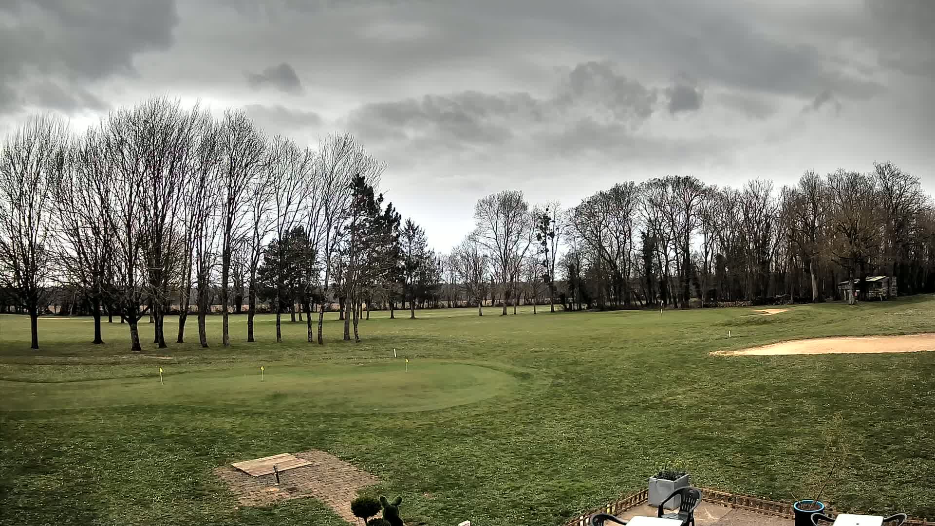 A golf course with leafless trees under a cloudy sky.