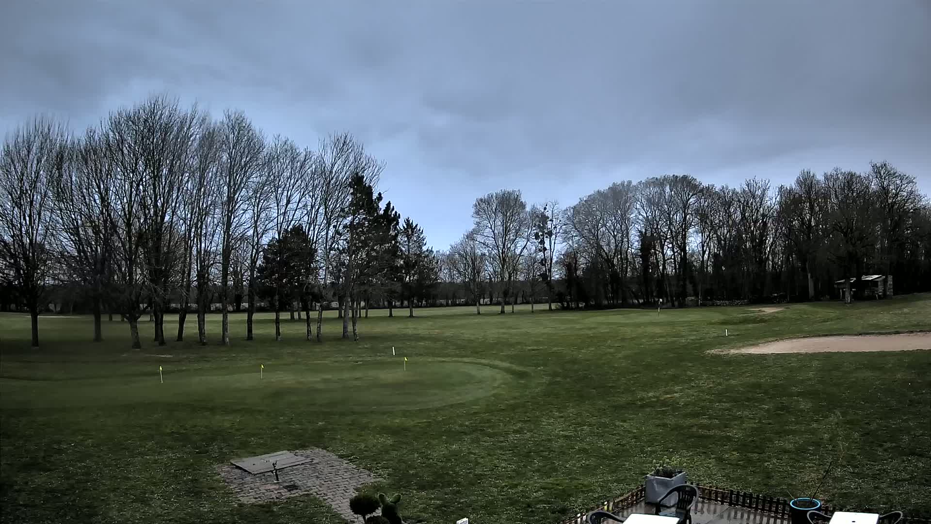 A golf course with bare trees under a cloudy sky.