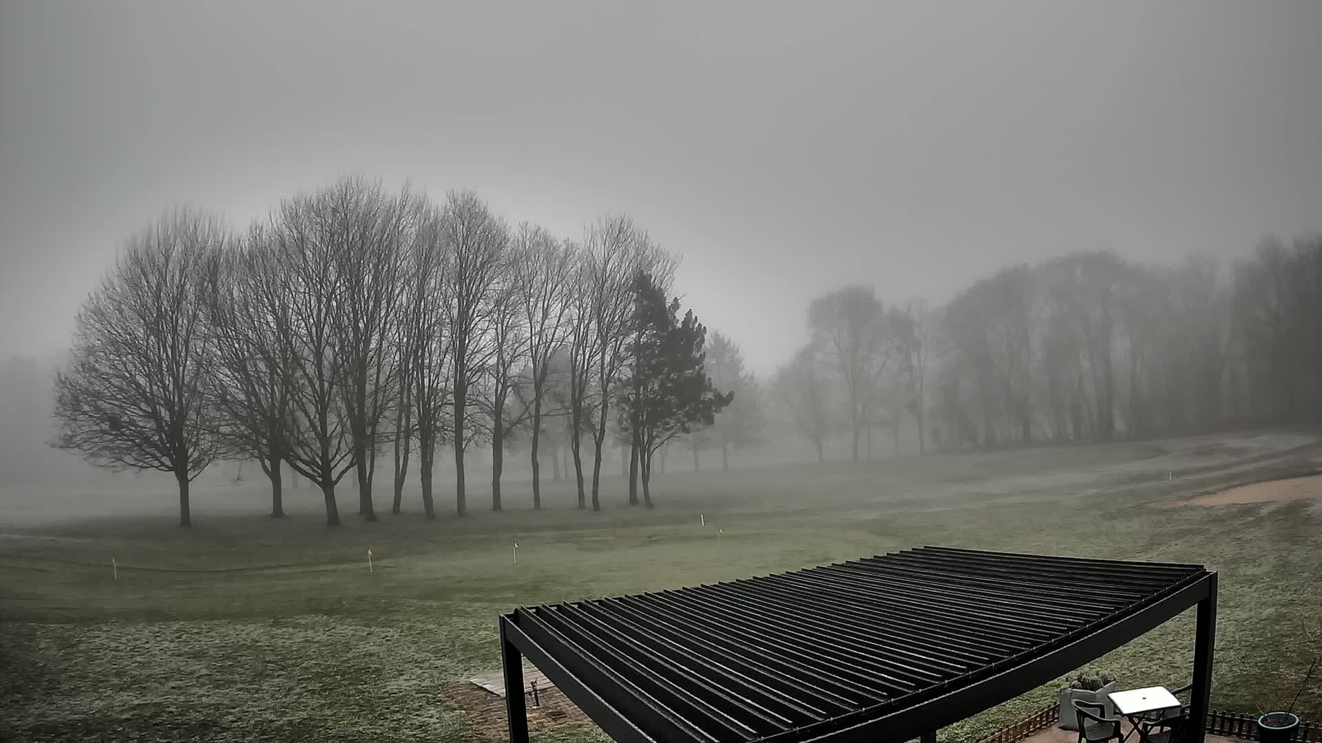 A foggy, frost-covered golf course is visible beyond a modern metal pergola.