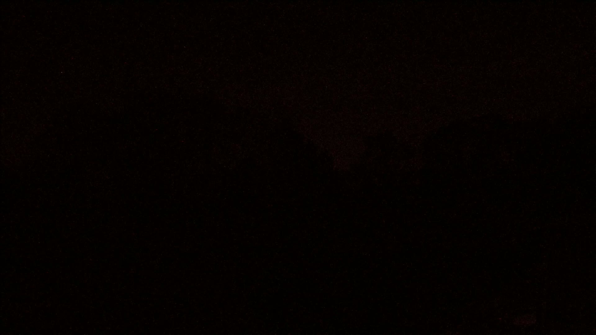 A mostly black image shows a dark, possibly nighttime scene with faint, indistinct shapes and a scattering of red-brown specks.