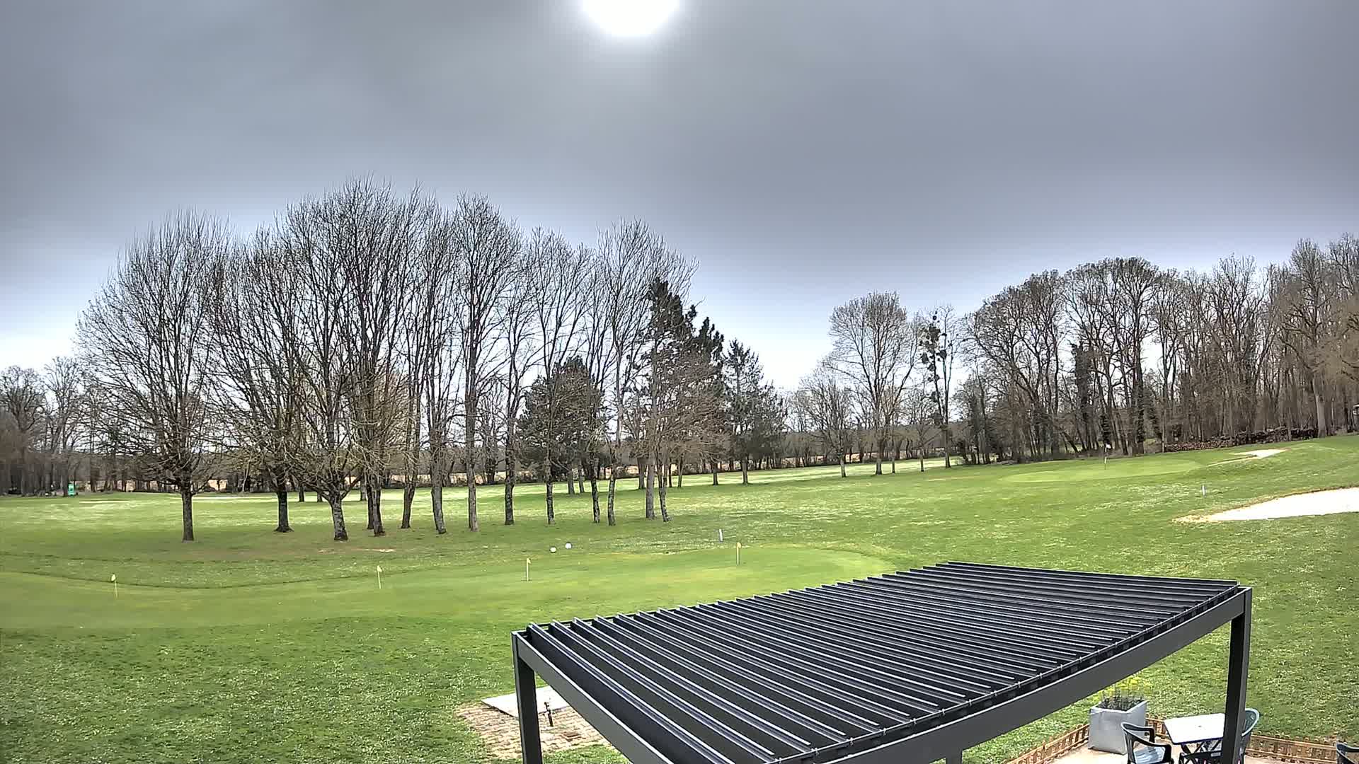 A partly sunny day overlooks a golf course with leafless trees and a modern pergola.