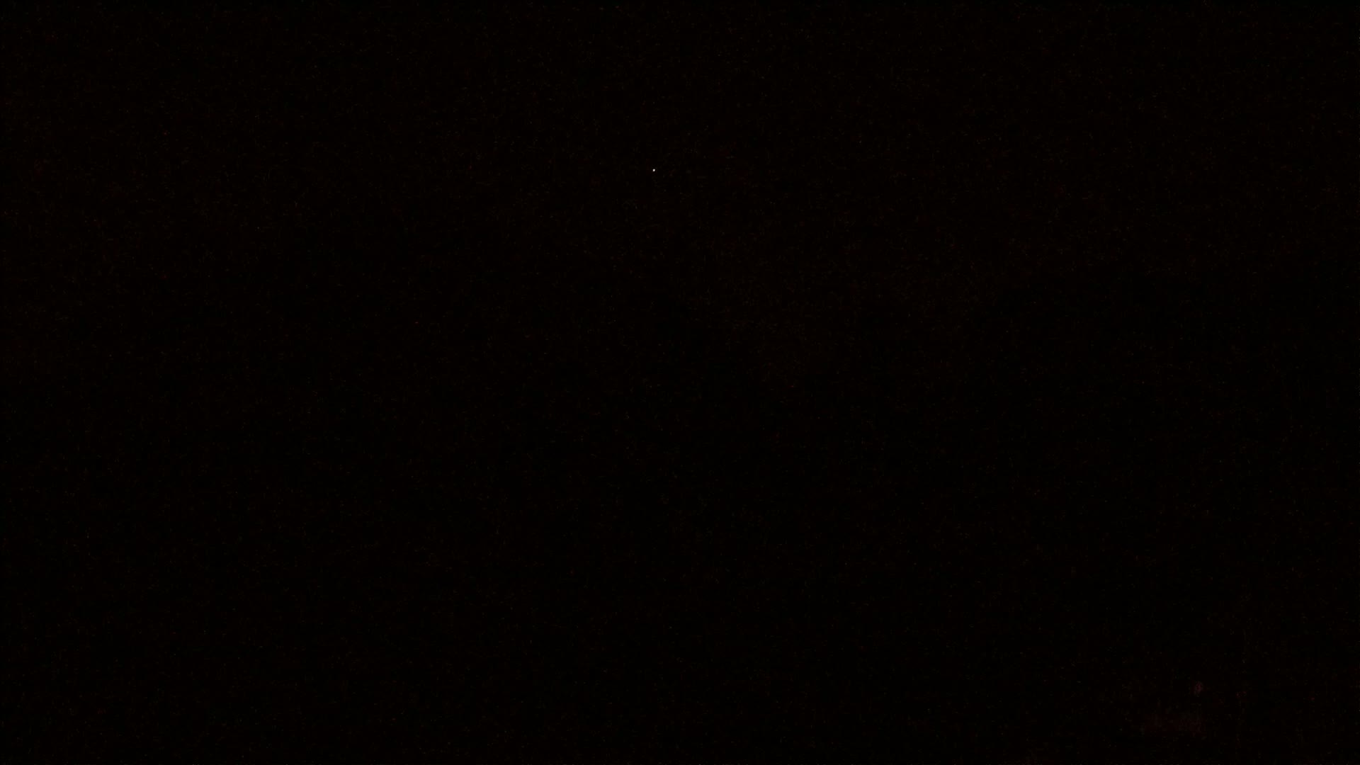 A nearly pitch-black image shows a few faint, scattered lights against a dark background.