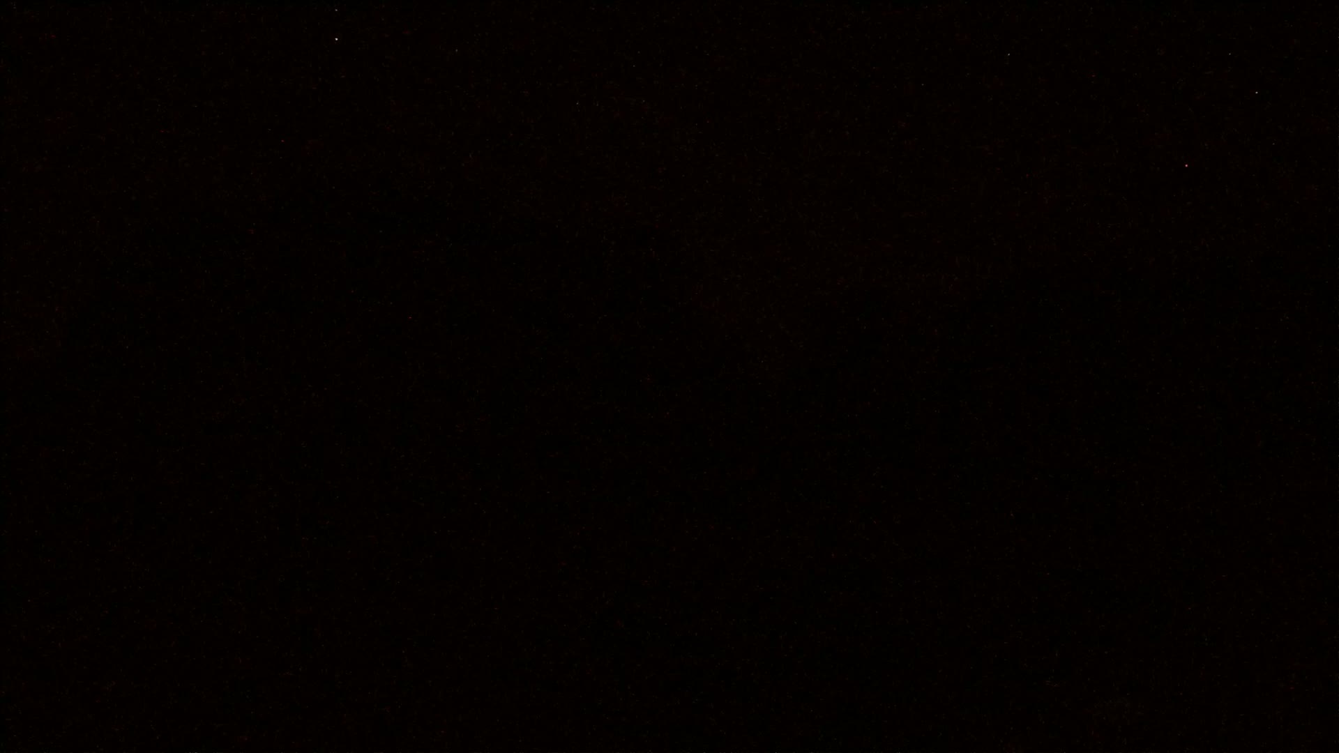 The image is an almost entirely black field with a few faint red specks scattered throughout.