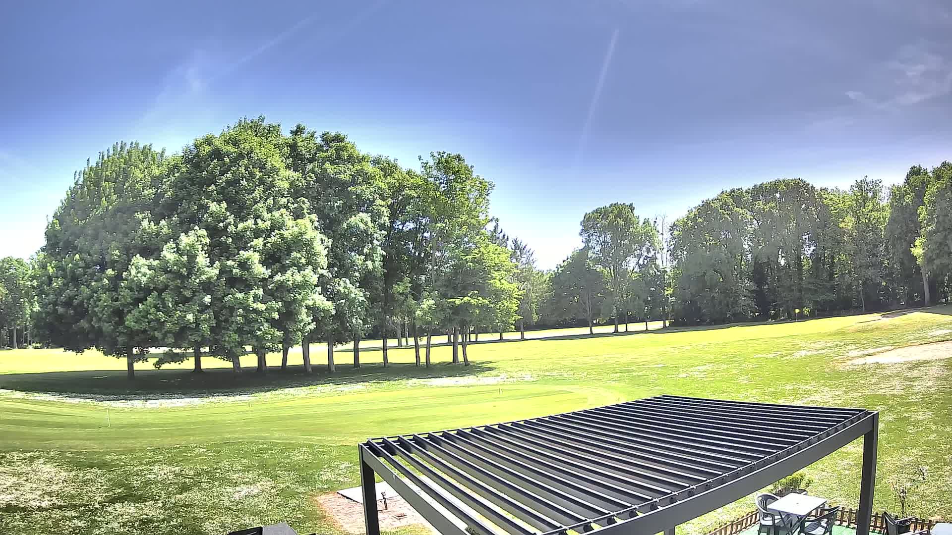 A grassy golf course is visible beyond a dark-colored pergola on a sunny day.