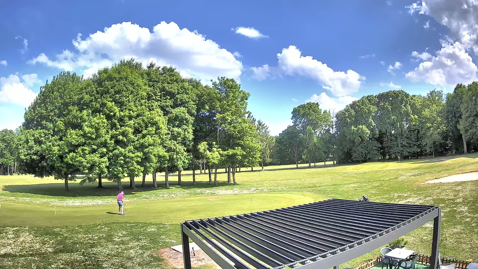 A golfer stands on a green golf course under a partly sunny sky with fluffy white clouds.