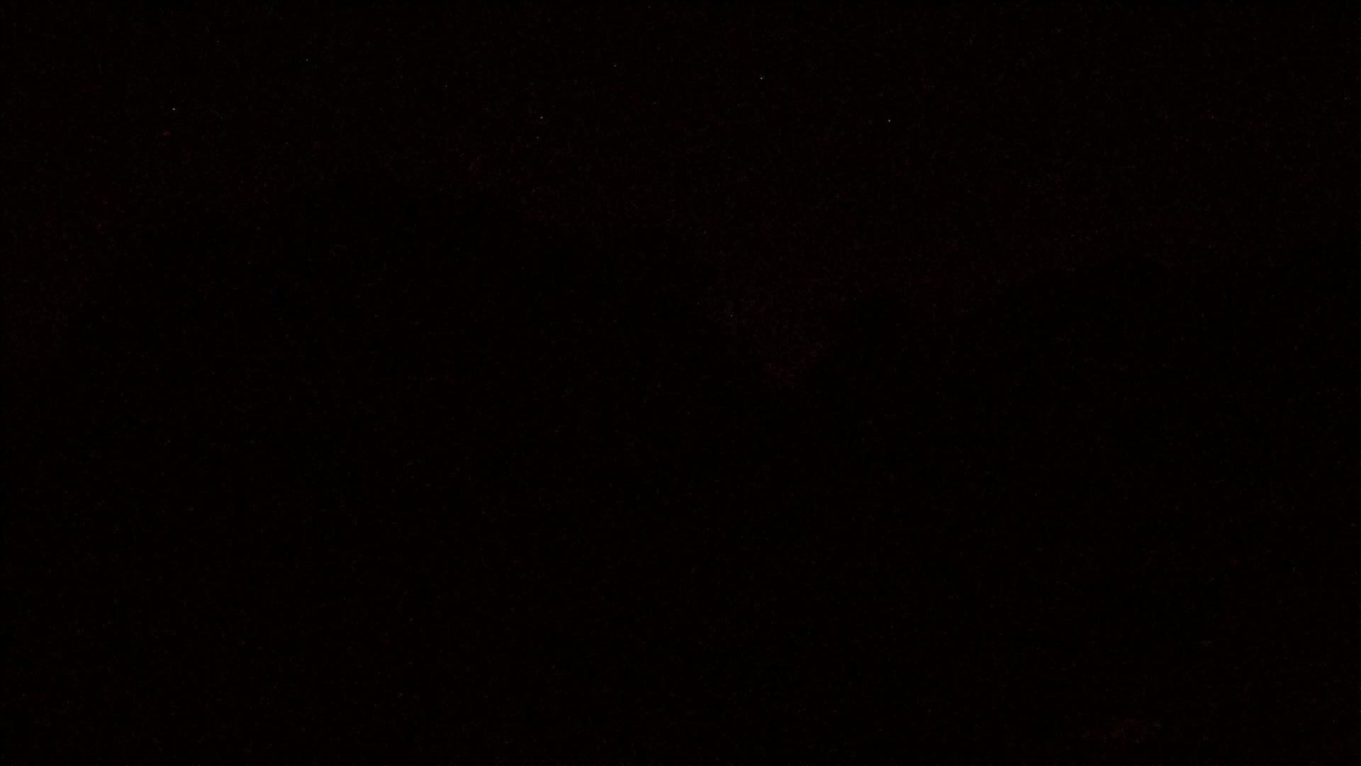 The image is a mostly black, slightly grainy background with sparse, faint red speckles.