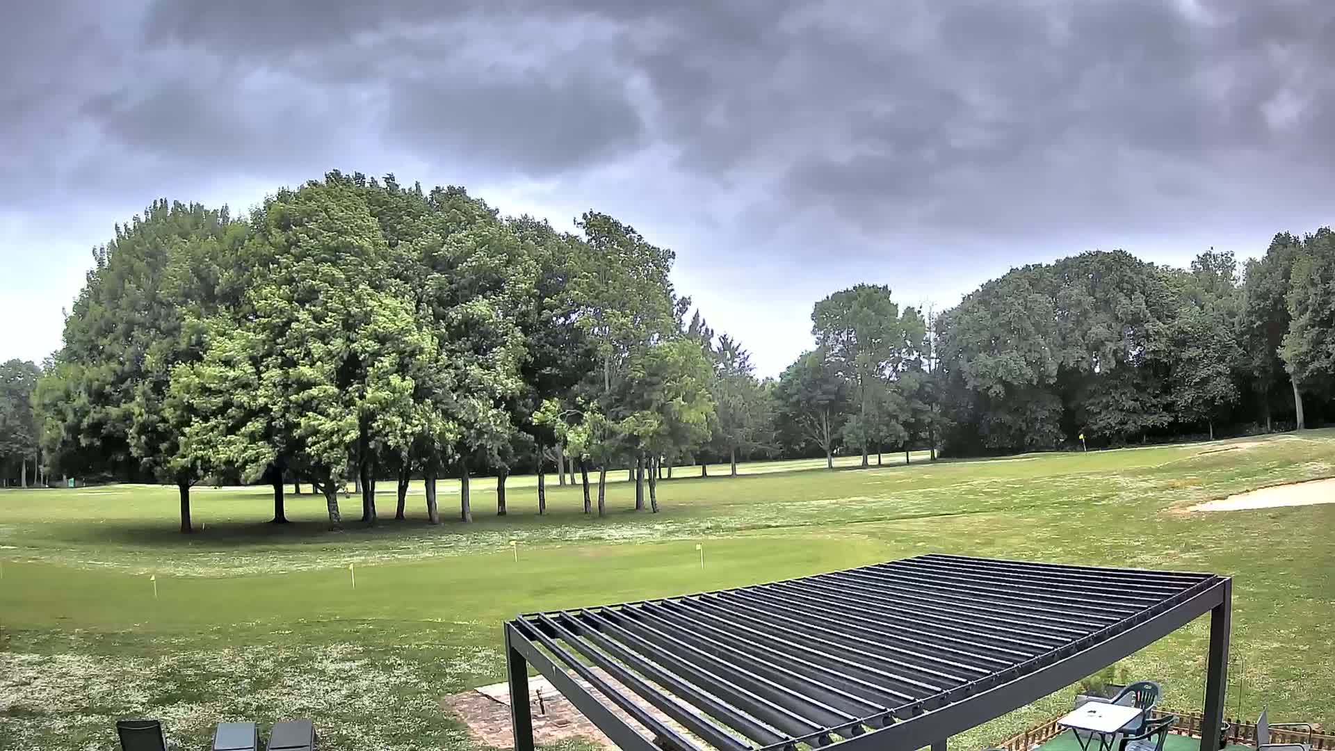 A golf course with a mostly cloudy sky is visible from a patio with a pergola.