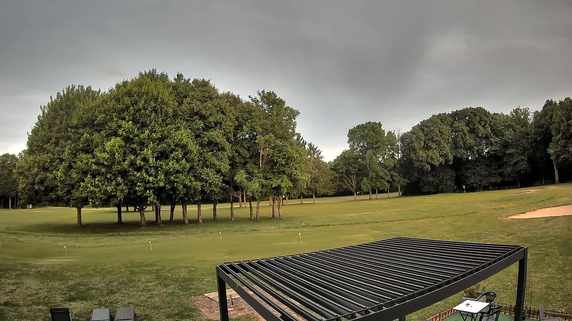 A golf course under a cloudy sky is partially visible from behind a dark metal pergola.