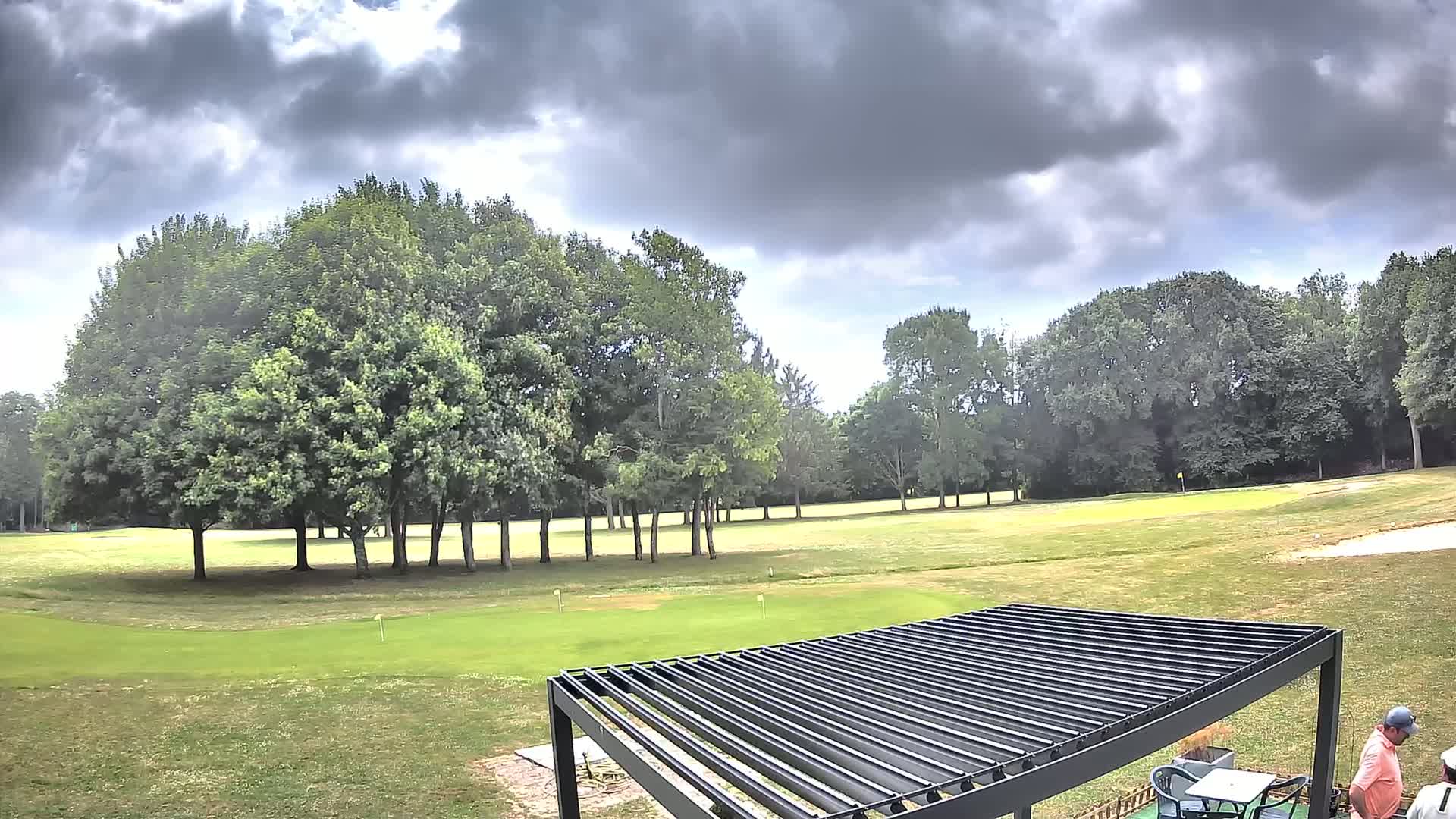 A golf course with a putting green and several green trees under a partly cloudy sky.