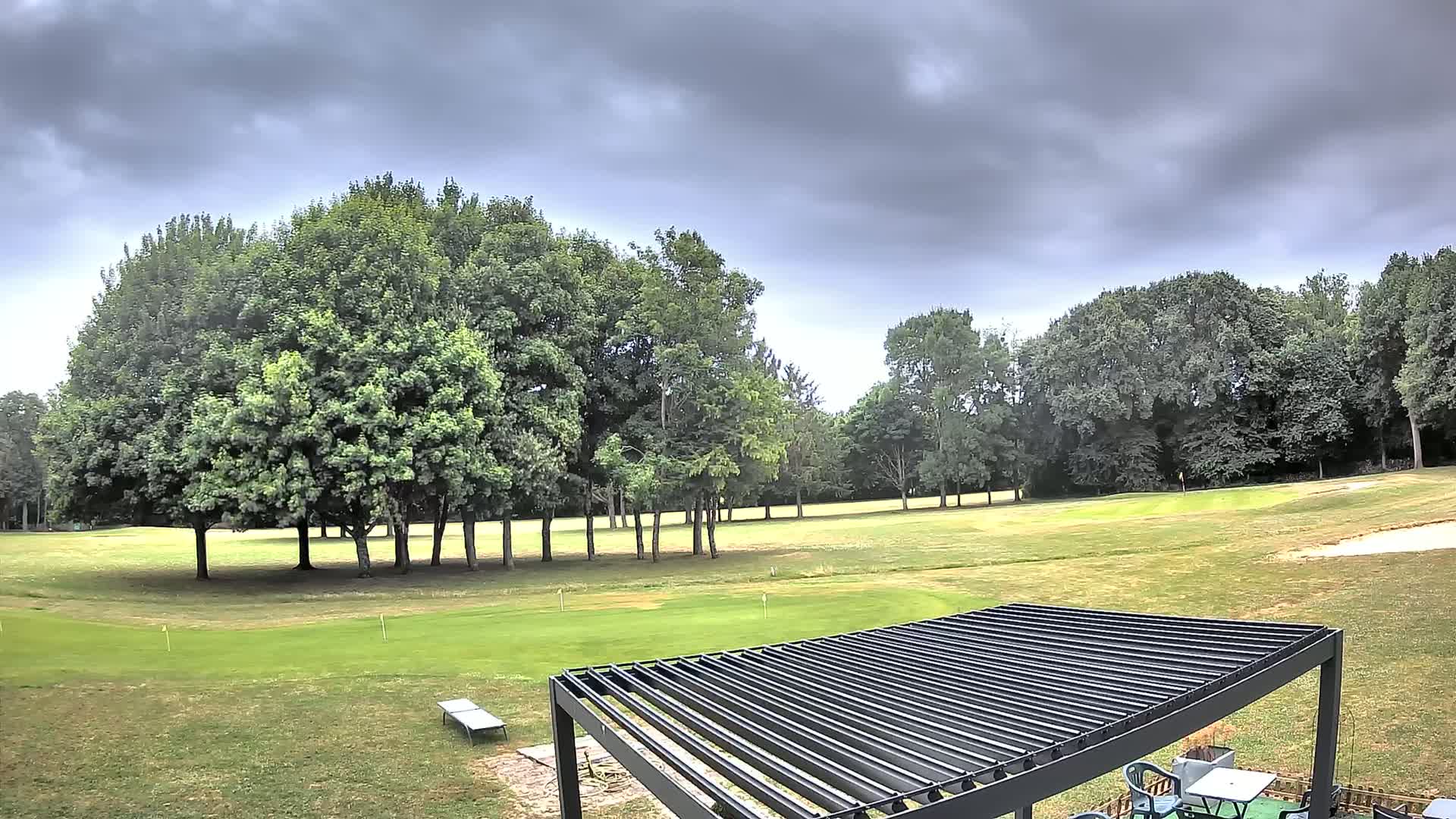 A golf course with a putting green and several trees under a cloudy sky.