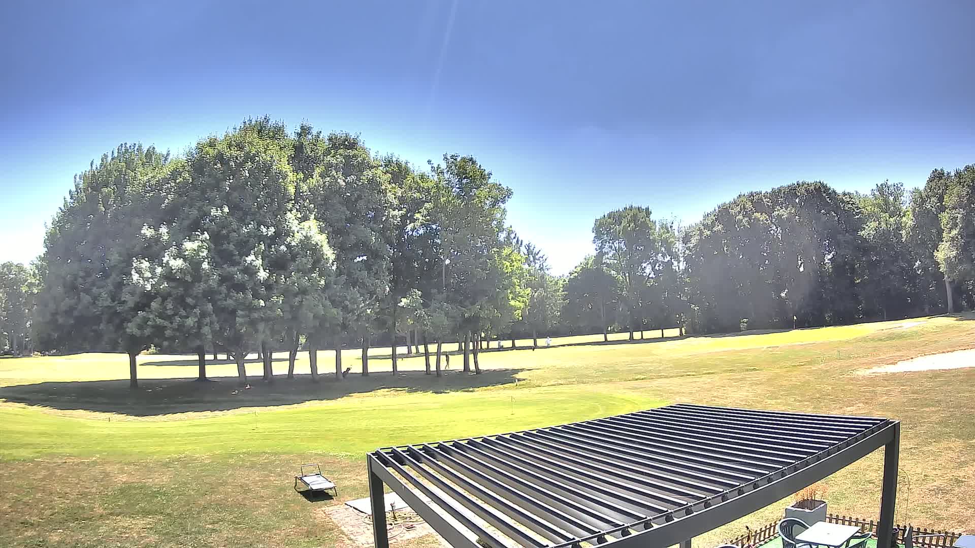 A grassy golf course is visible beyond a modern pergola on a sunny day.
