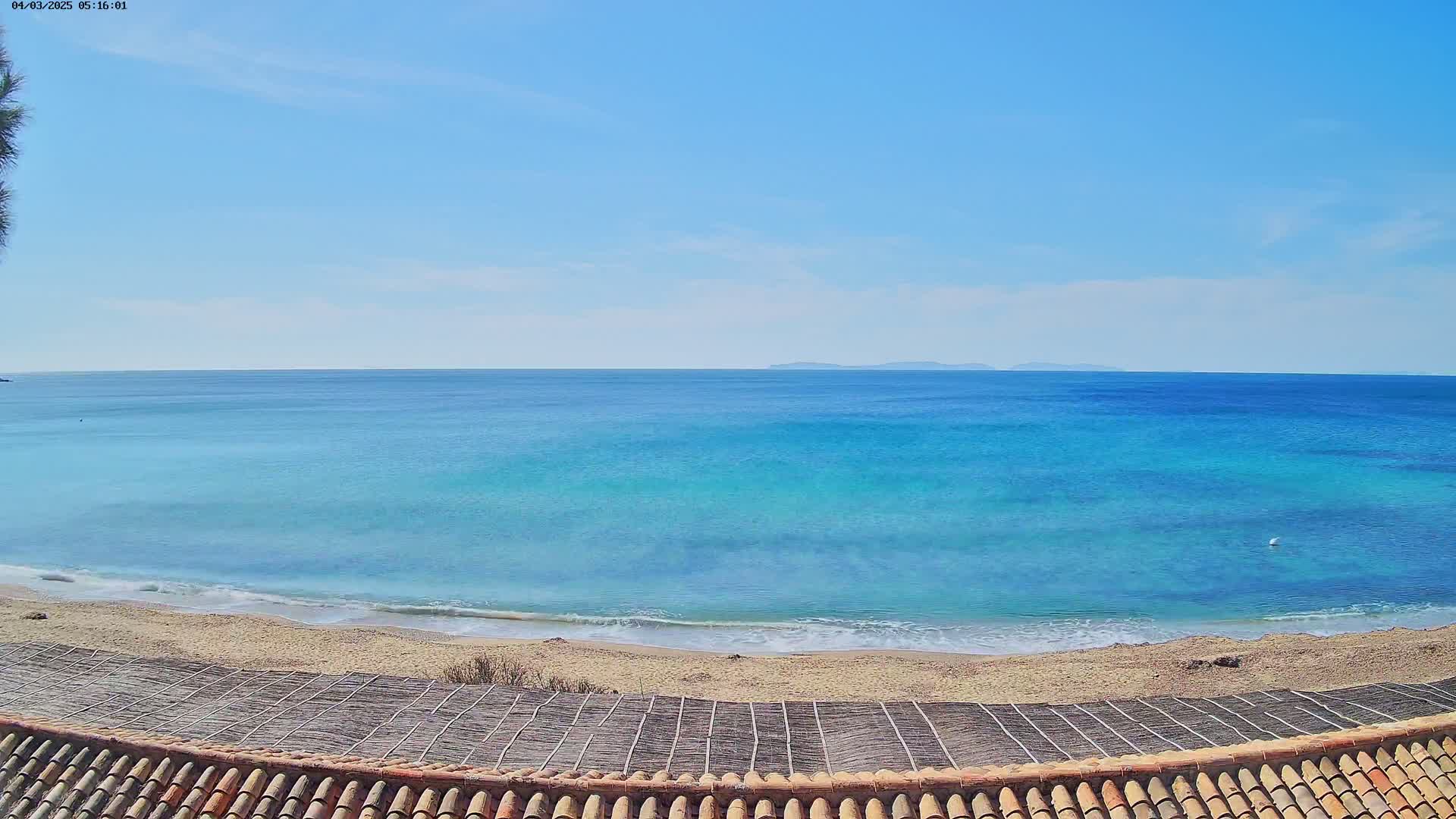 A sandy beach with calm, turquoise water under a clear blue sky meets a distant landmass.