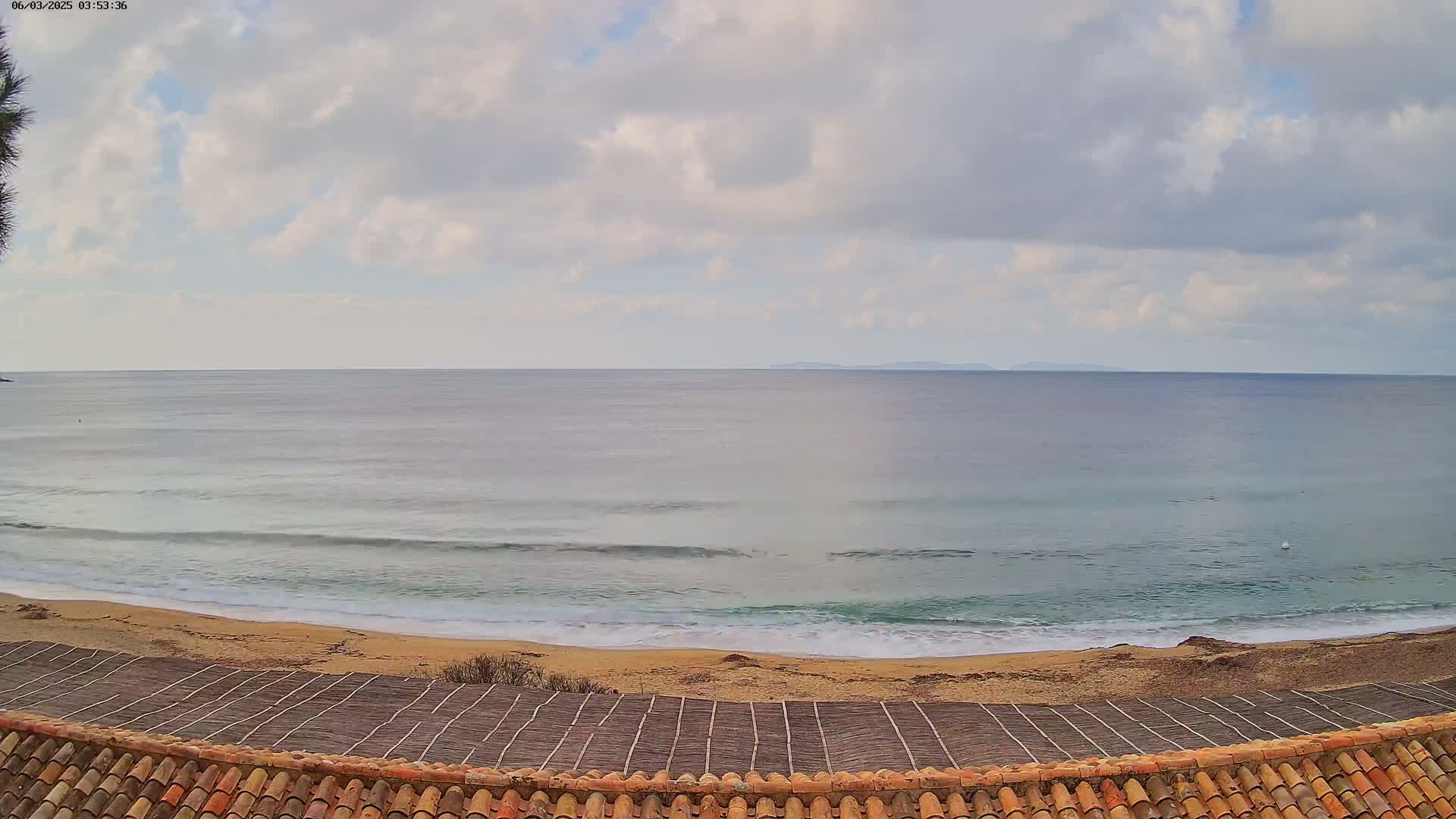 A sandy beach with gentle waves under a cloudy sky overlooks a calm ocean with a distant landmass.