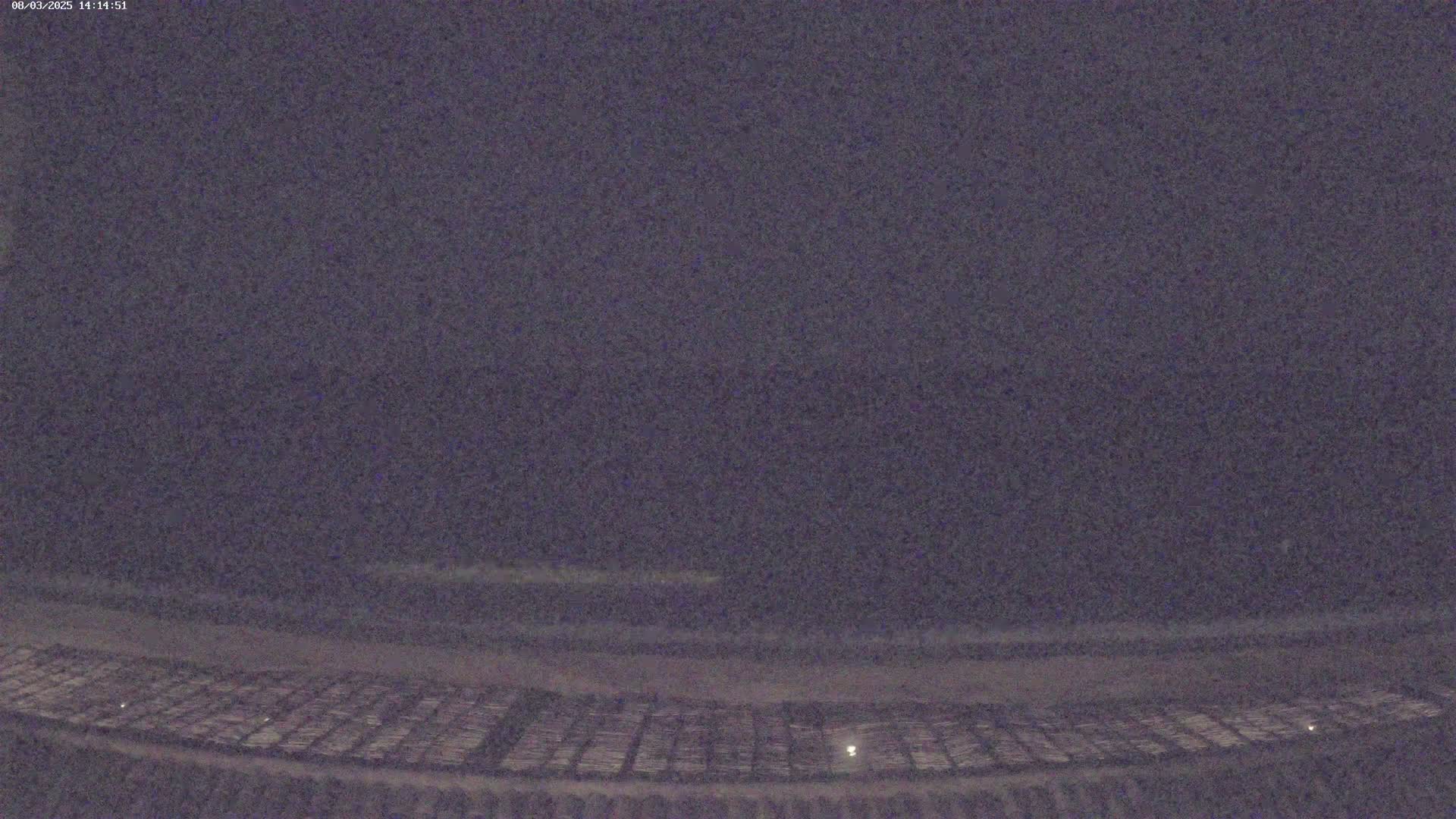 A dark, nighttime view shows a flat, expansive area of what appears to be a field or parking lot with faintly visible grid patterns.