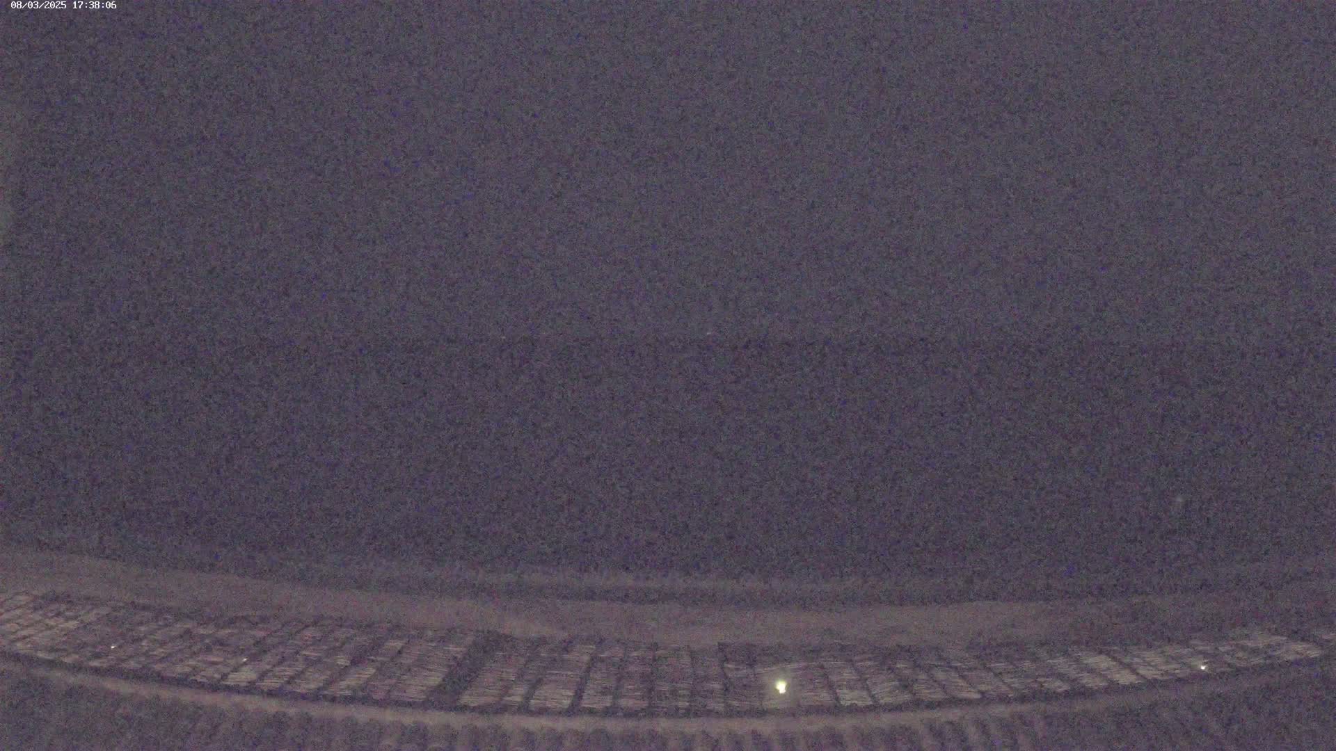 A low-light nighttime image shows a large, flat, dark area with a grid pattern at the bottom, under a dark, overcast sky.