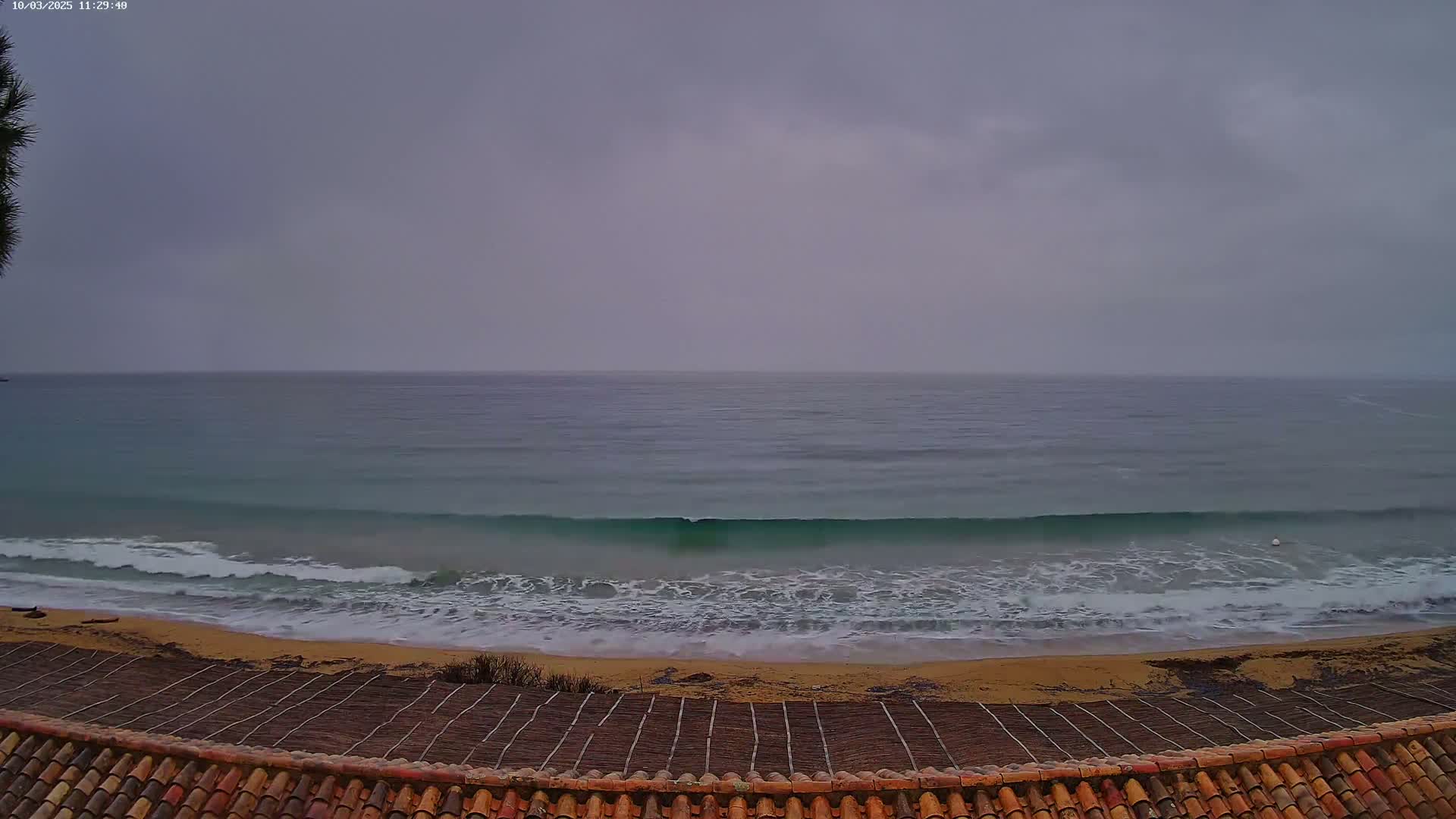 A sandy beach with gentle waves rolls onto the shore under an overcast sky.