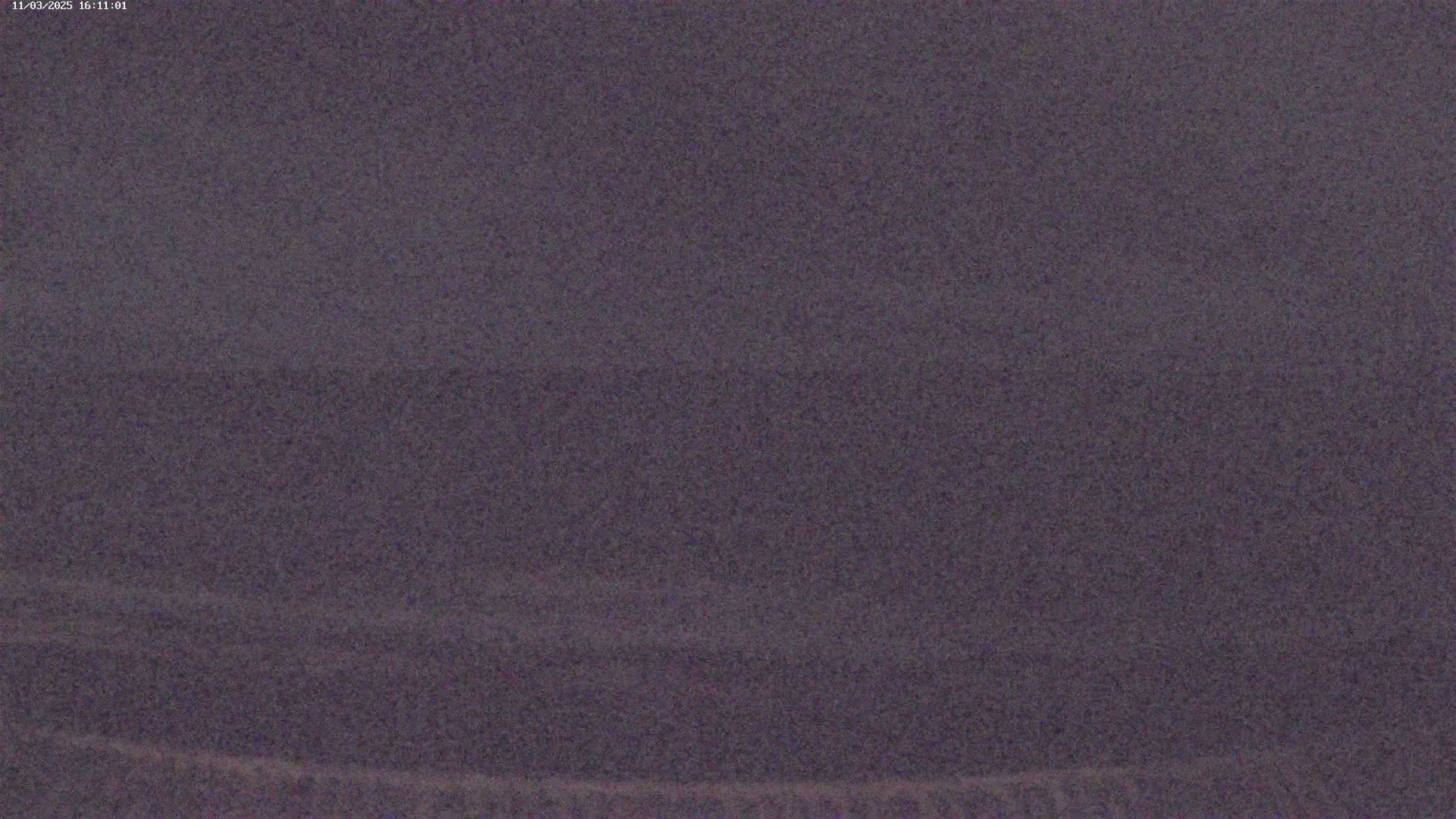 A grainy, dark purple image shows an indistinct, possibly nighttime, outdoor scene with low visibility.