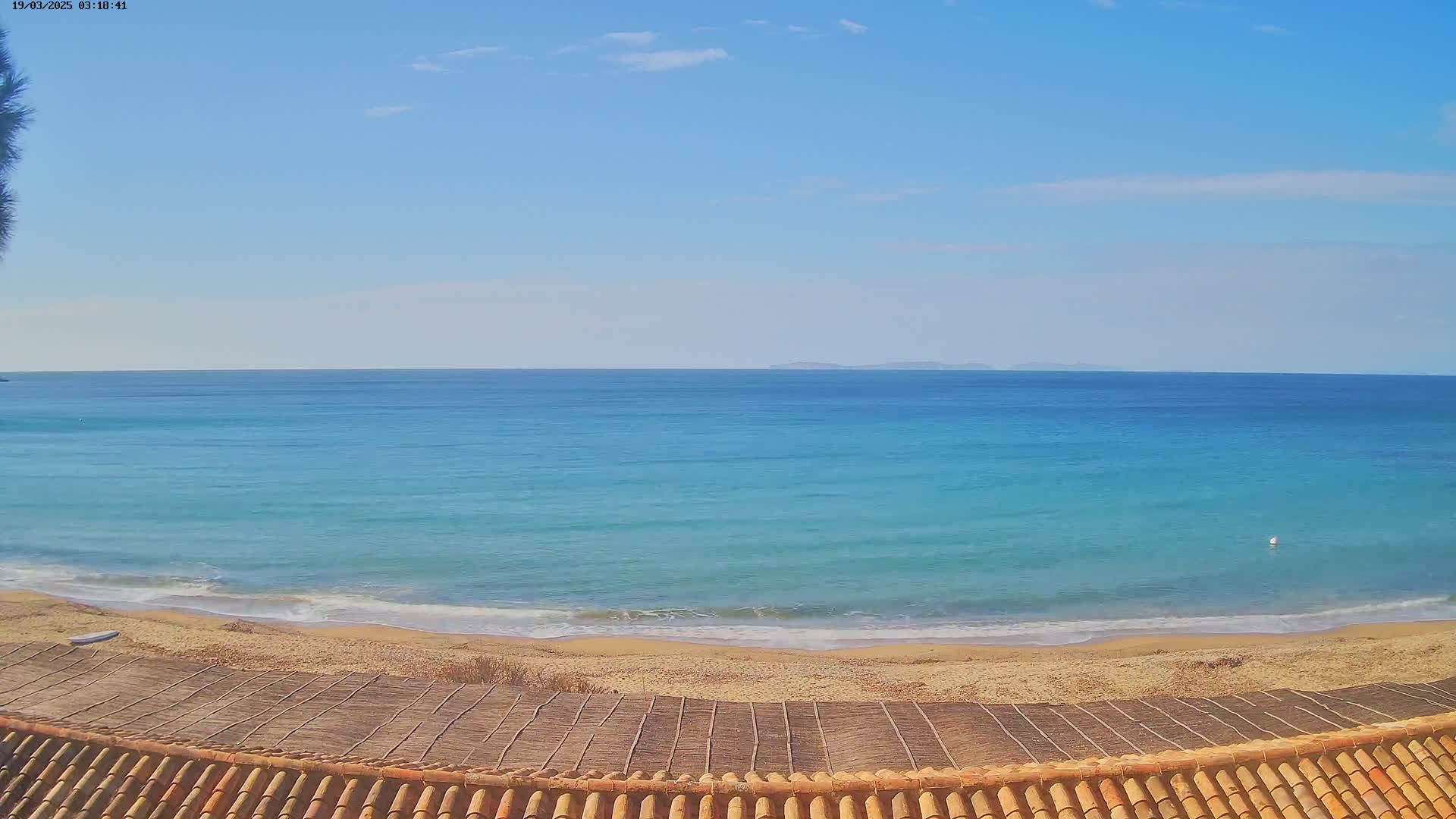 A sandy beach meets a calm, turquoise ocean under a clear blue sky.