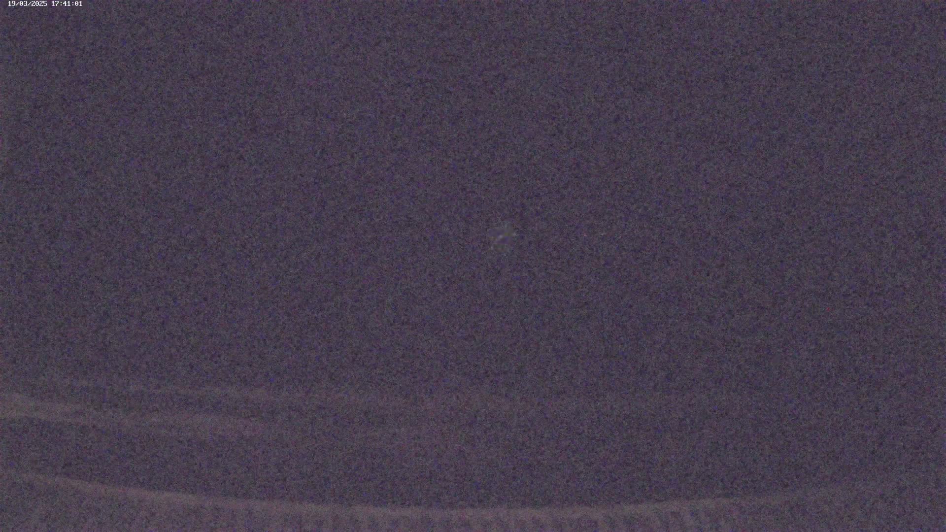 A dark purple, grainy image shows a mostly clear night sky.