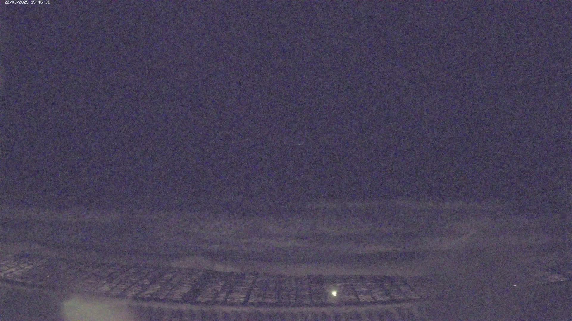 A nighttime, low-light view of a flat, textured surface, possibly a field, under a dark, cloudy sky.