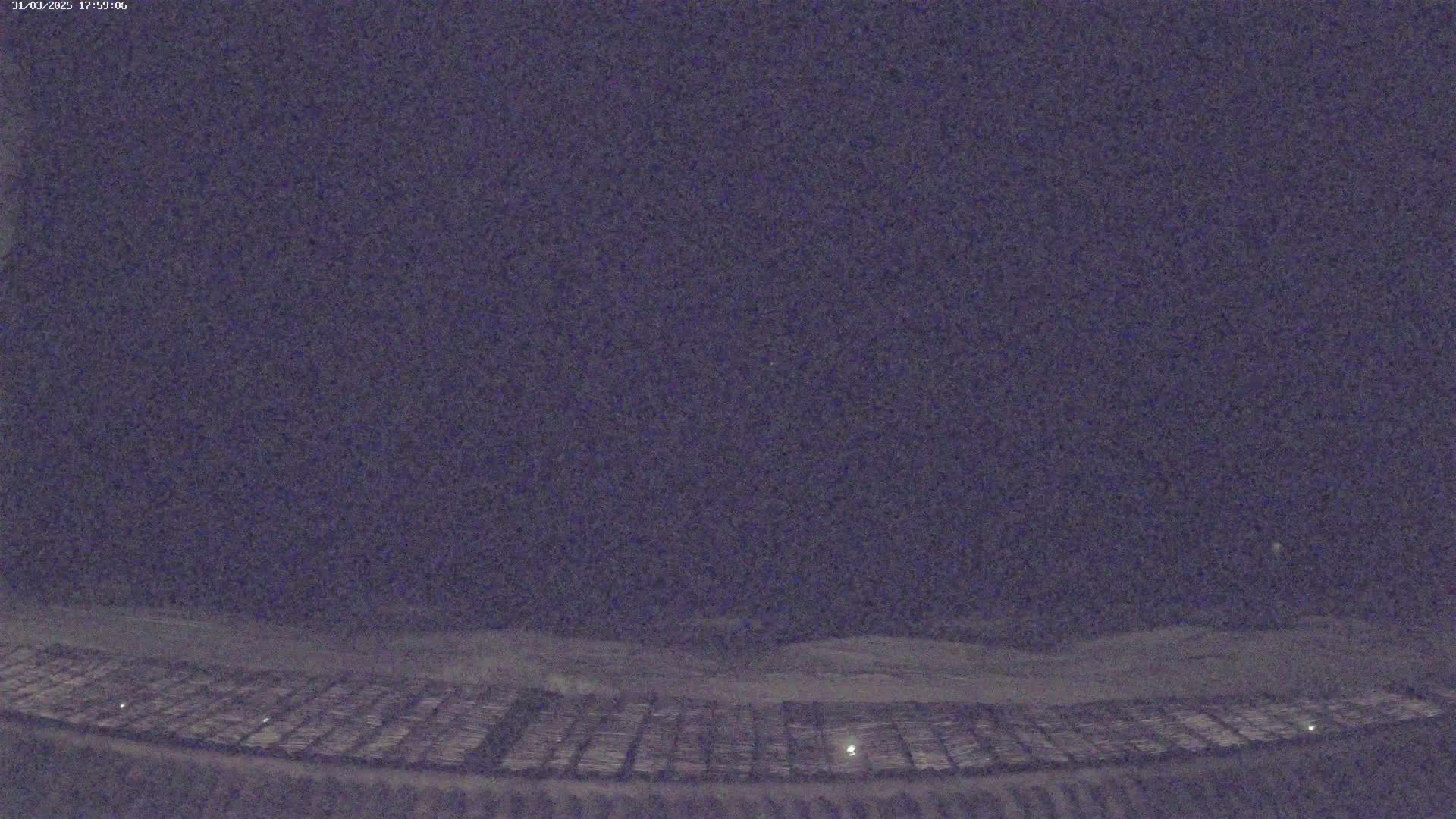 A nighttime view of a snow-covered, grid-like field under a dark, clear sky.
