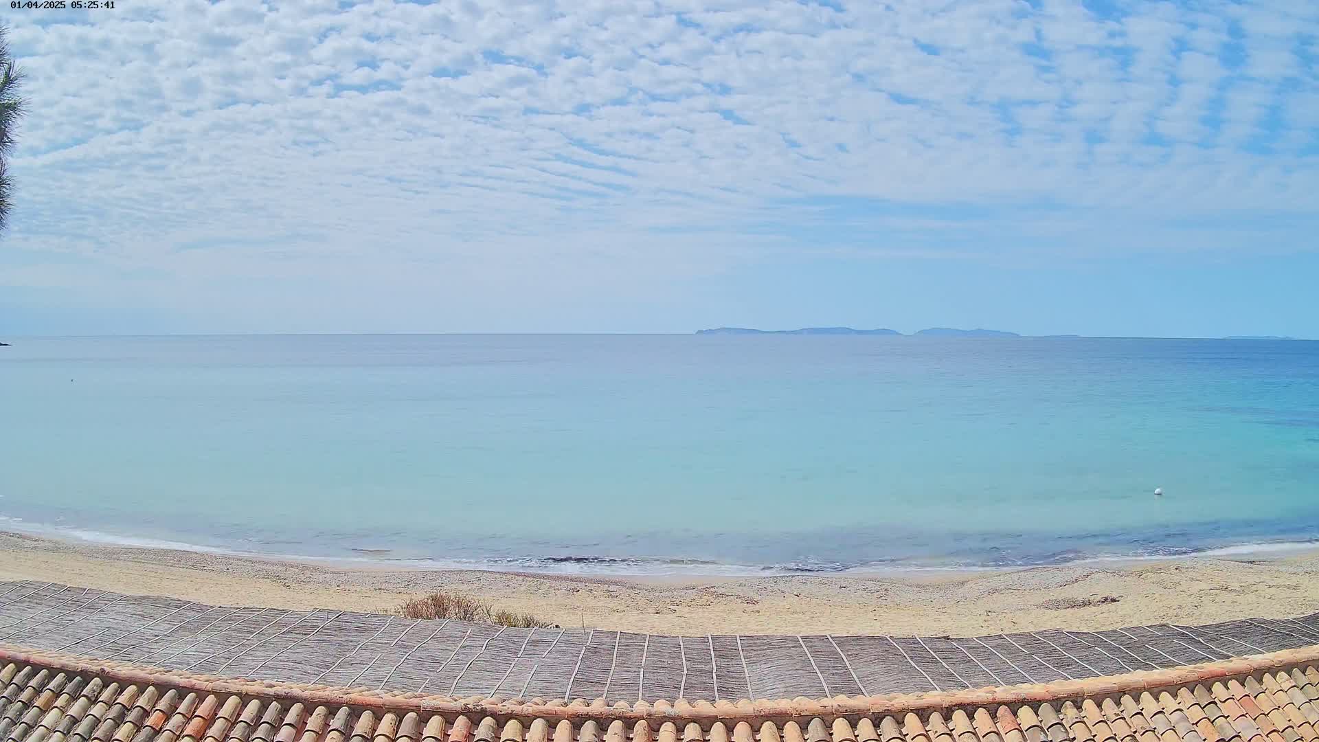 A sandy beach with light blue-green water stretches to a distant landmass under a partly cloudy sky.
