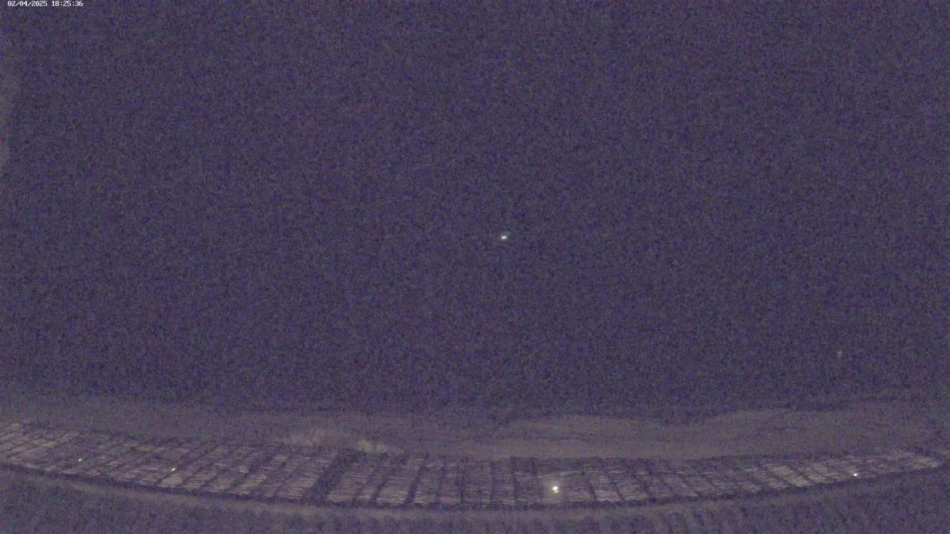 A nighttime view shows a vast, dark field with faint lights, a single bright light visible in the dark sky above.
