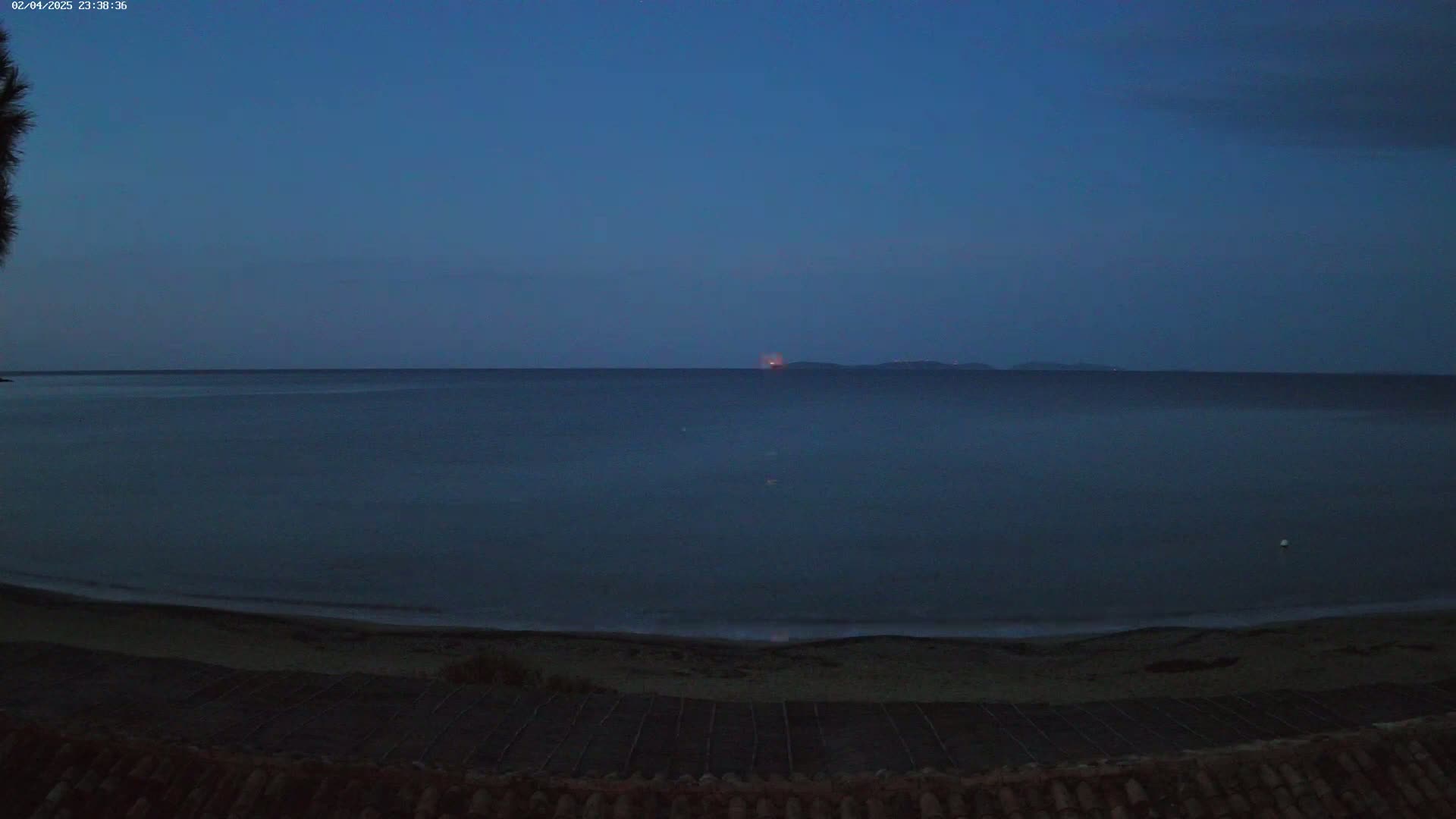 A dark, calm sea meets a dark sandy beach under a twilight sky.