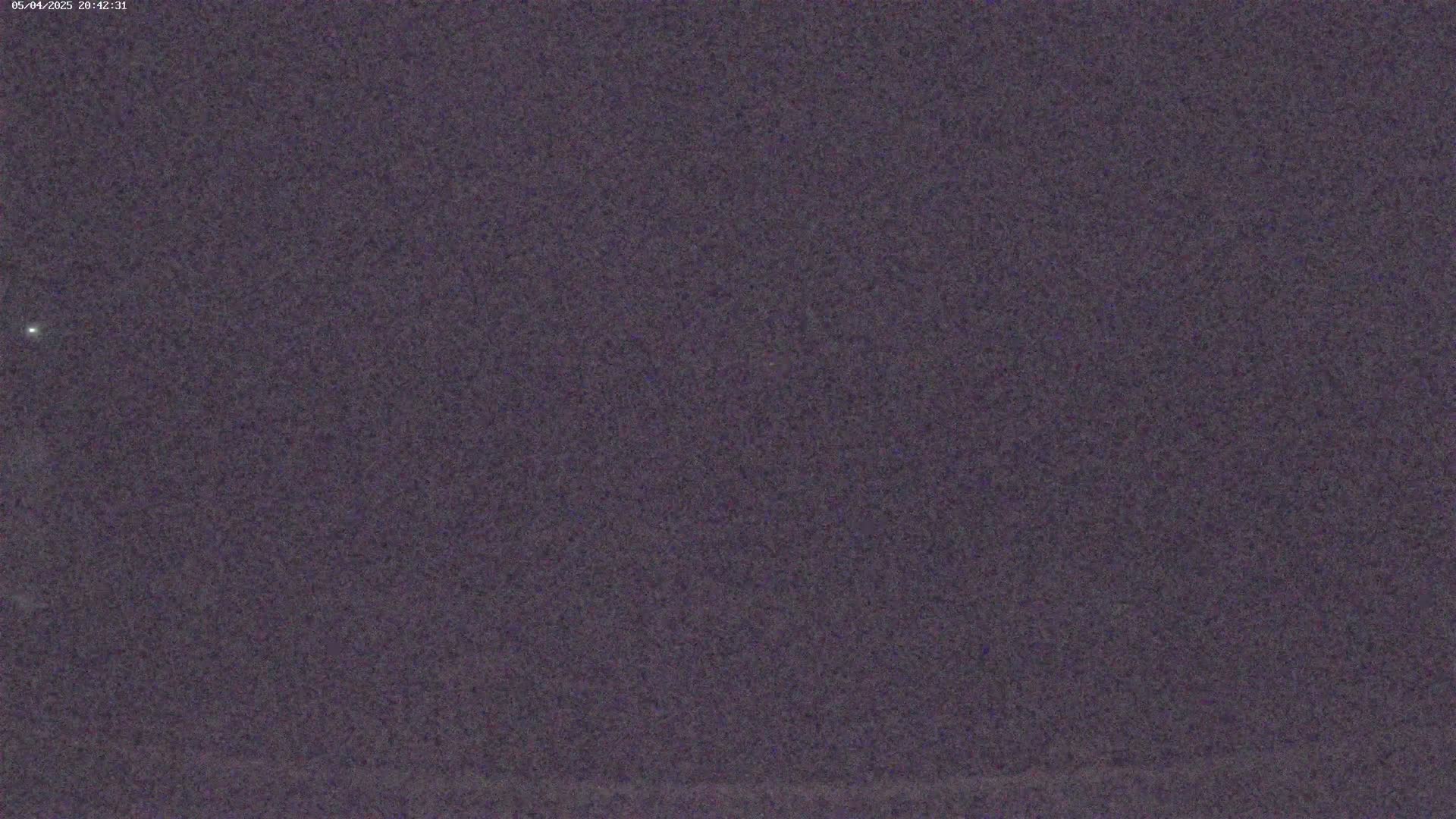 A dark, grainy nighttime image shows a mostly clear sky with a single, faint light visible.