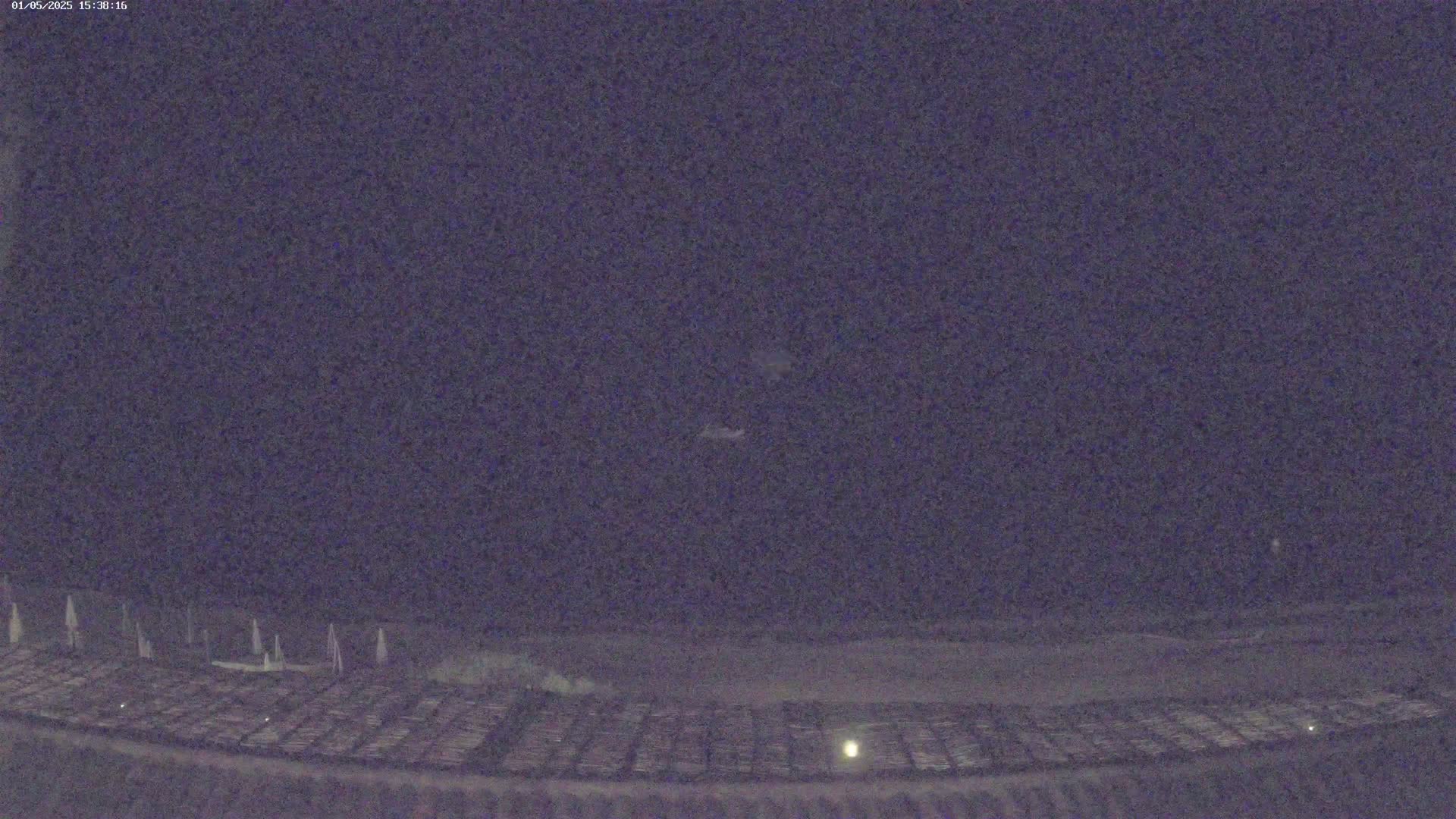 A low-light nighttime image shows a dark expanse of land with what appears to be a parking lot or similar arrangement of spaces, and a few faint lights visible in the distance.