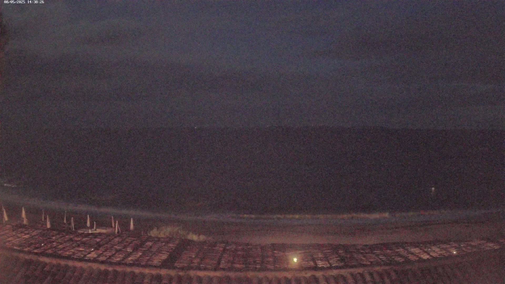 A dark beach at night, with a dark body of water beyond it, under a mostly clear, dark sky.