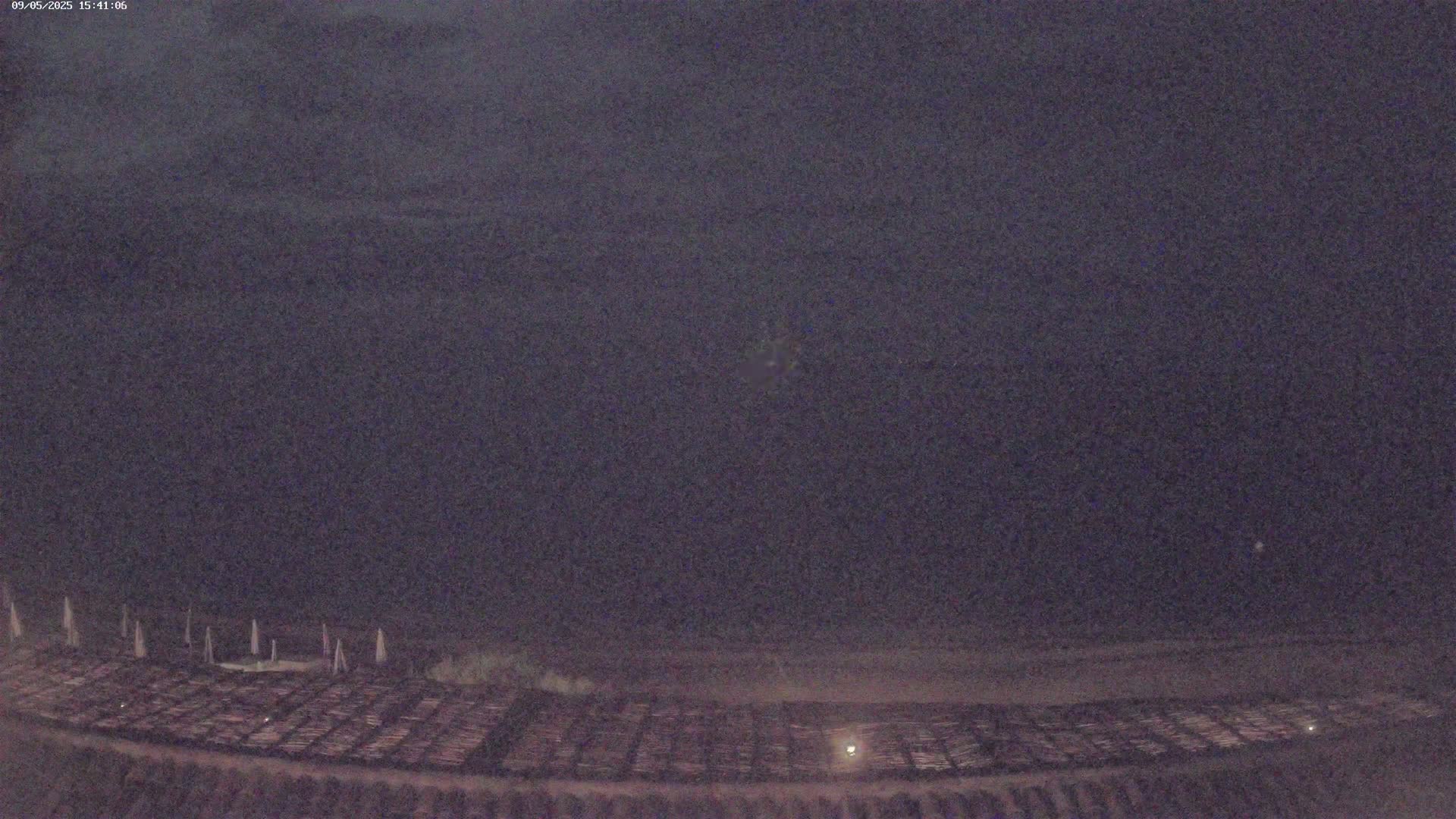A dark, nighttime view shows a large, flat area covered with what appears to be a grid of evenly spaced objects under a mostly clear, dark sky.