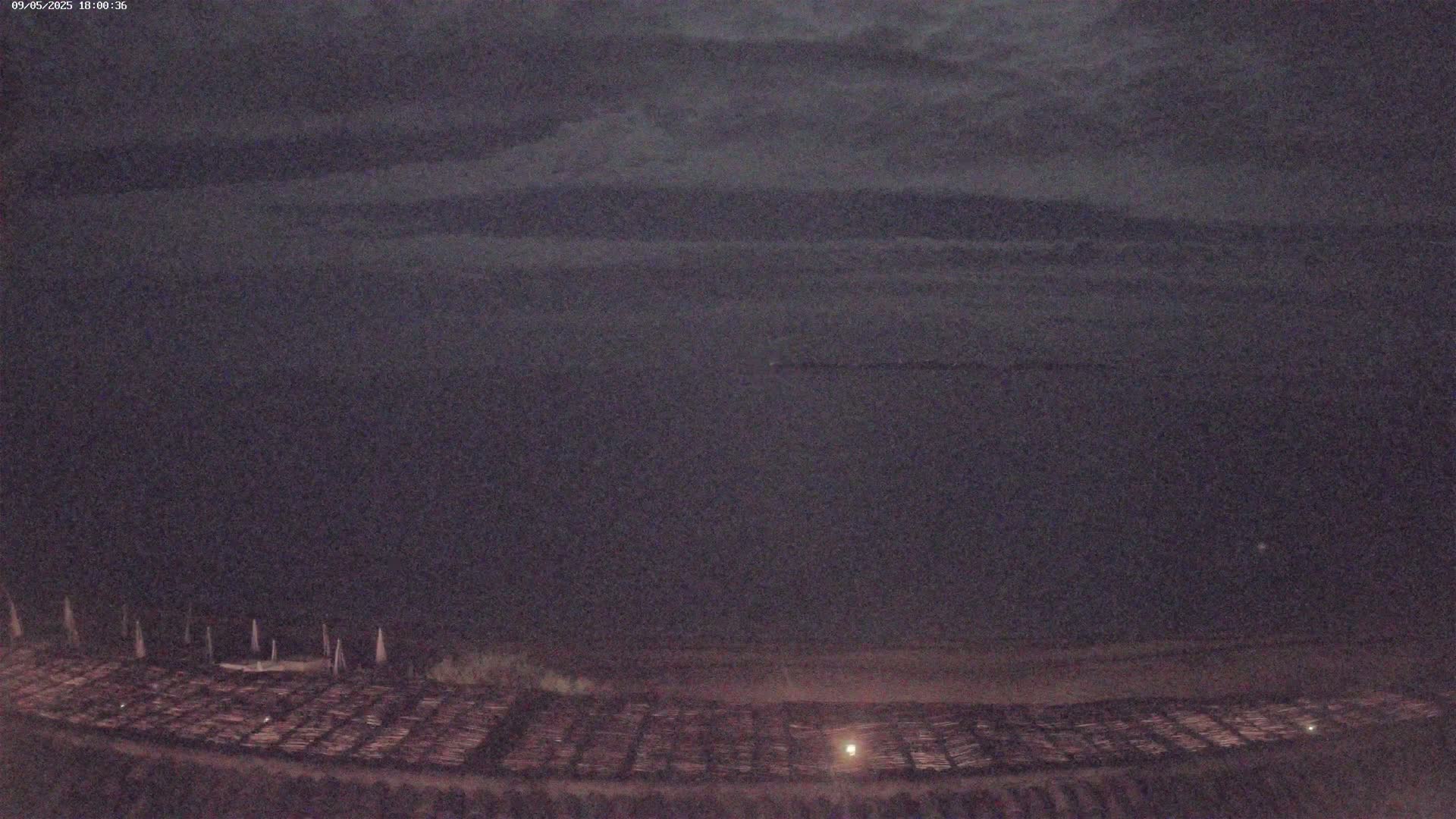 A dark, nighttime scene shows a large expanse of dark water under a cloudy sky, with a ground-level area in the foreground containing many neatly arranged, long, narrow objects.