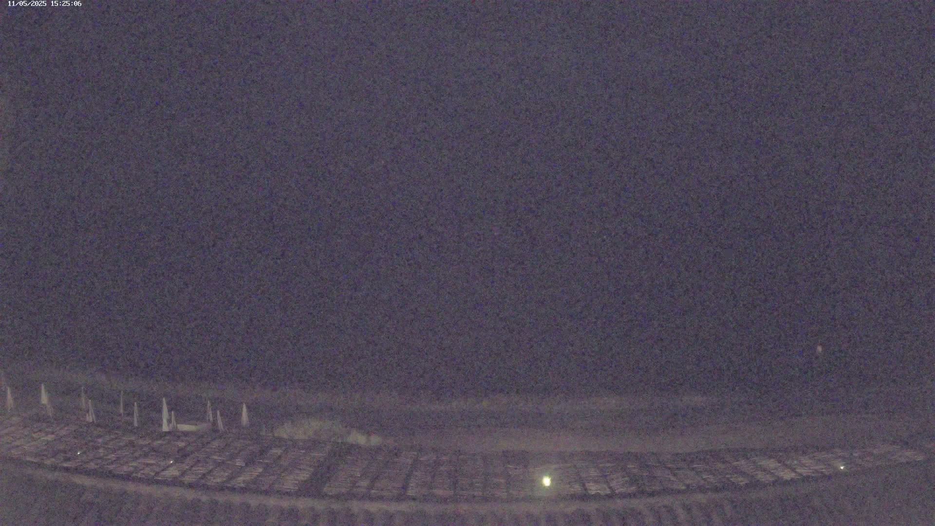 A dark, nighttime scene shows a large, flat area with many evenly spaced objects, possibly arranged in rows, under a mostly clear, dark sky.