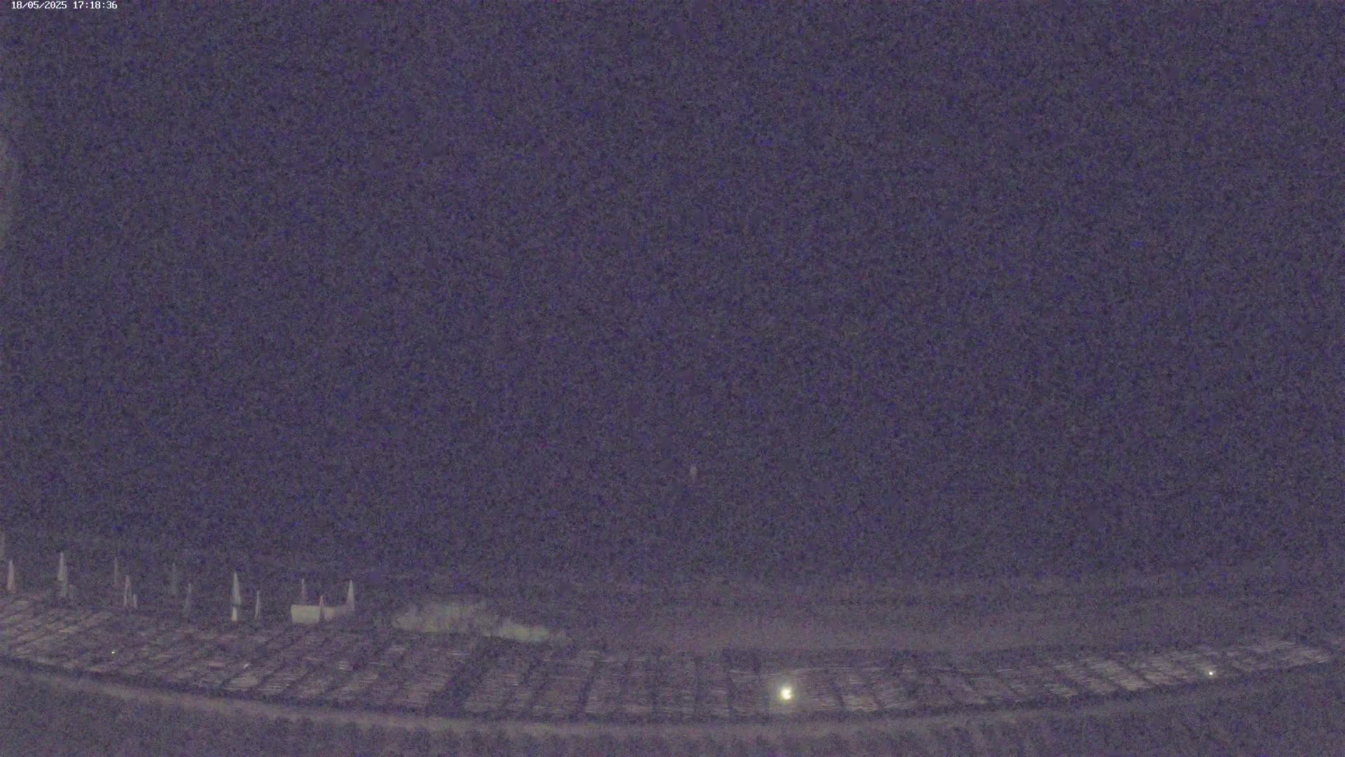 A nighttime, low-light view shows a large, flat, dark area with rows of objects, possibly vehicles, under a dark, clear sky.