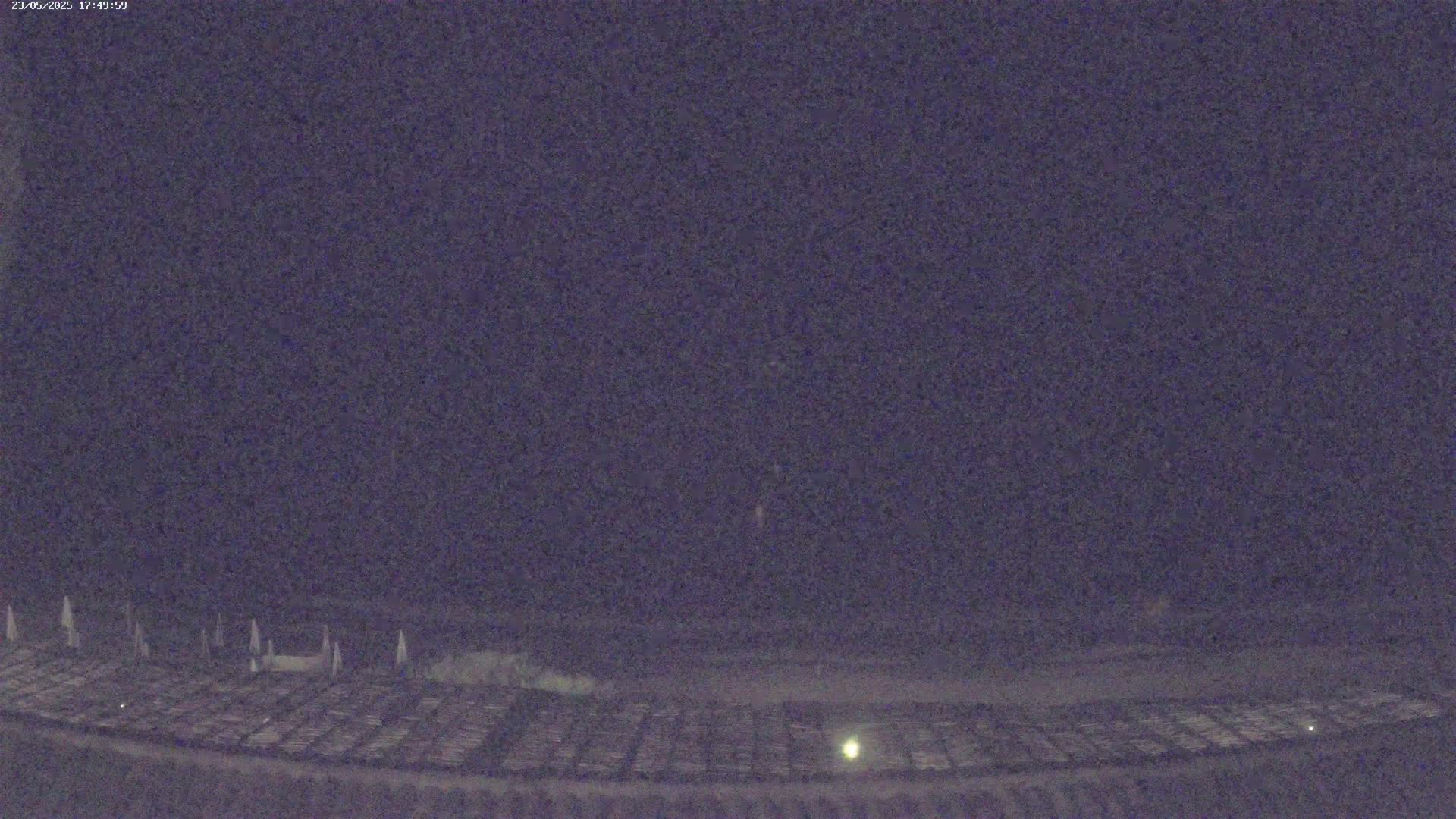 A nighttime, low-light view shows a dark, expansive area with a pattern of regularly spaced objects on the ground.