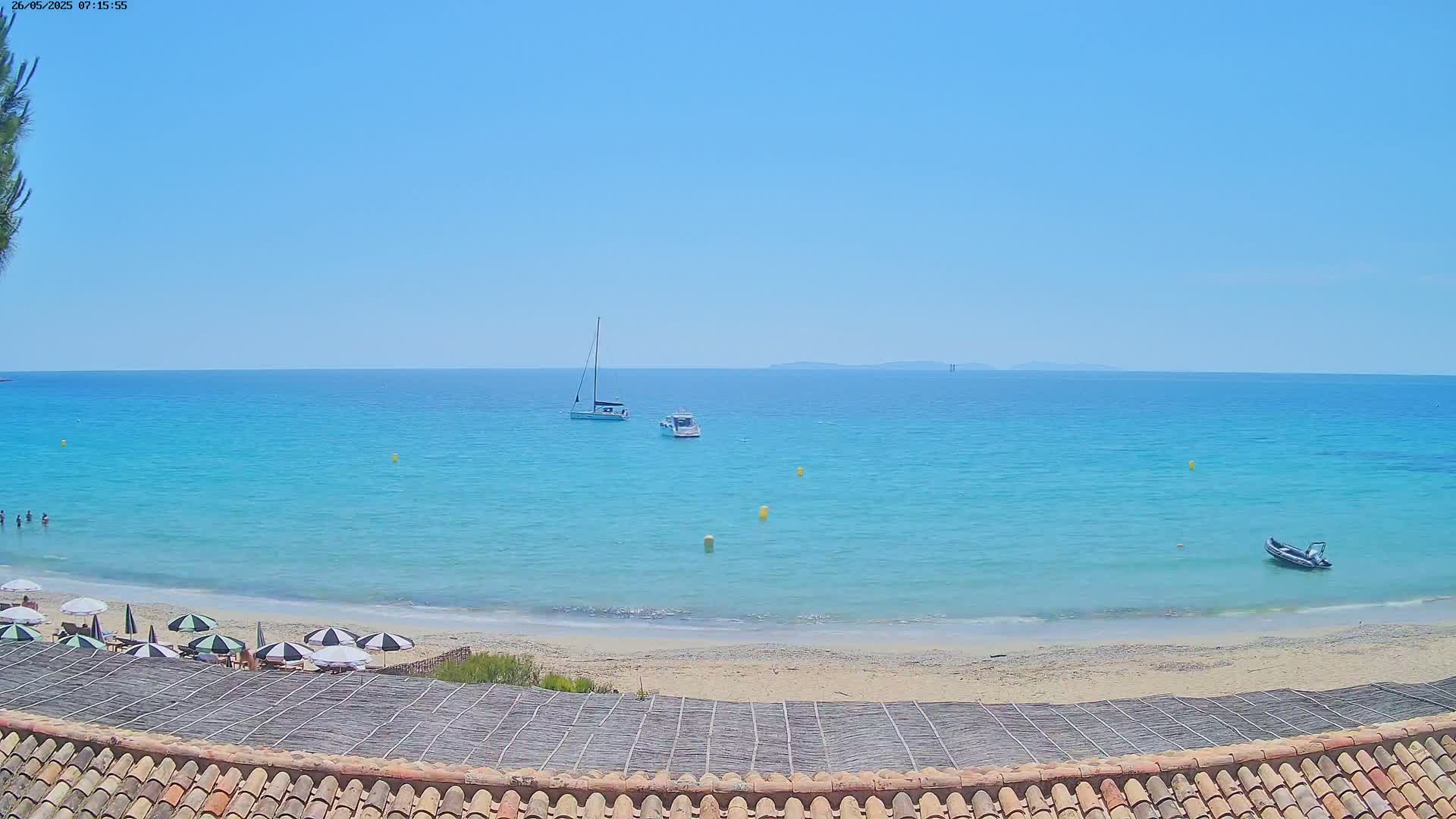 A sandy beach with turquoise water, several boats, and a few beach umbrellas under a clear blue sky.