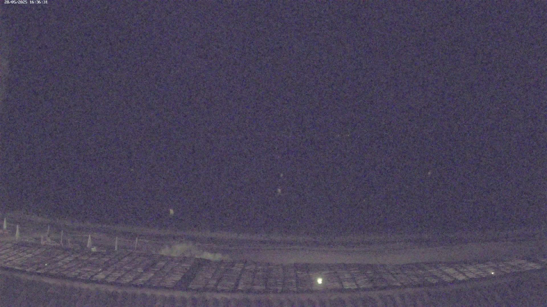 Under a dark night sky, a large, grid-like ground area is visible, with a few faint lights scattered across it.