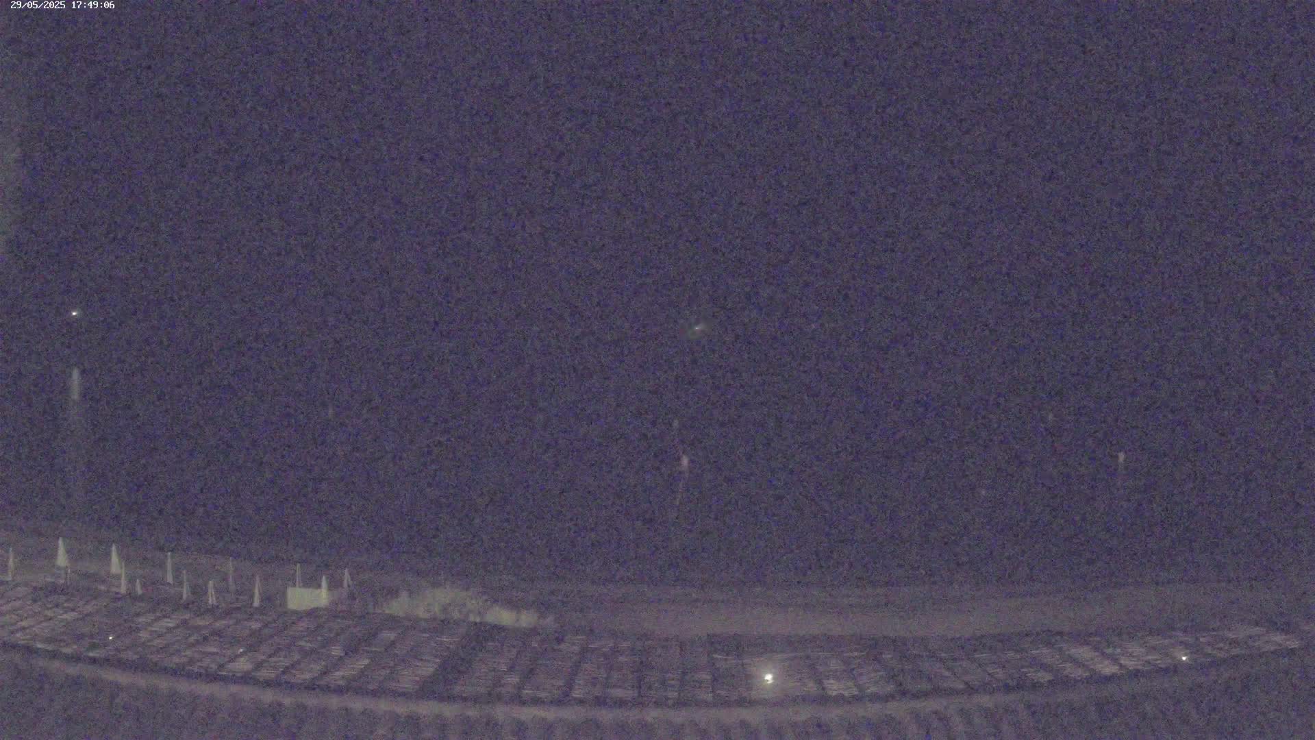 A nighttime view shows a large, dark area with faint lights and what appears to be a long, thin streak of light in the night sky.